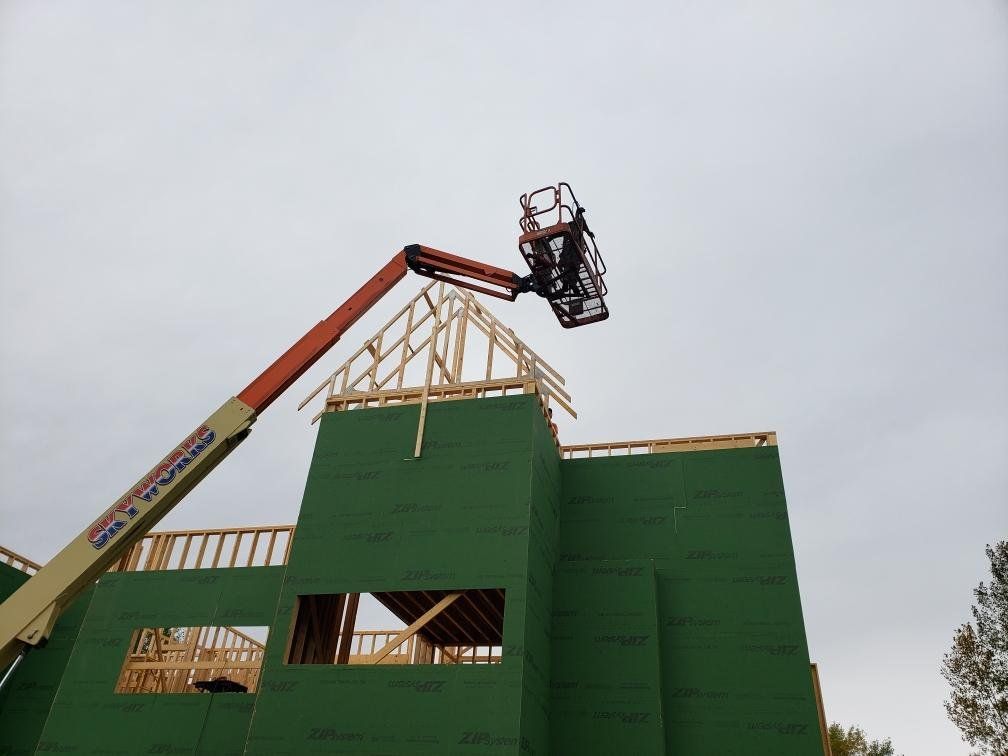 Crane lifting workers above a green building under construction