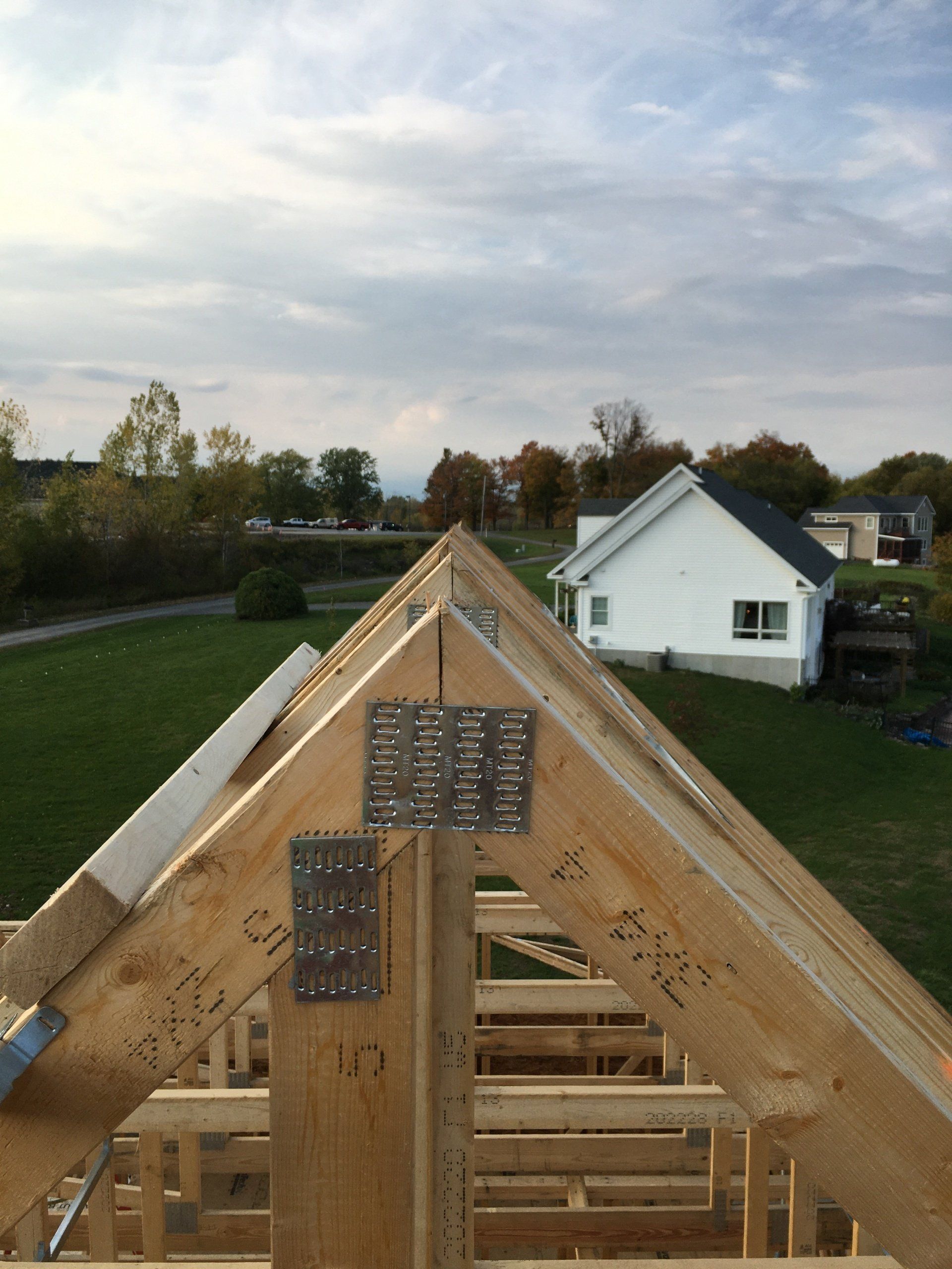 Roof trusses under construction with a house and cloudy sky in the background