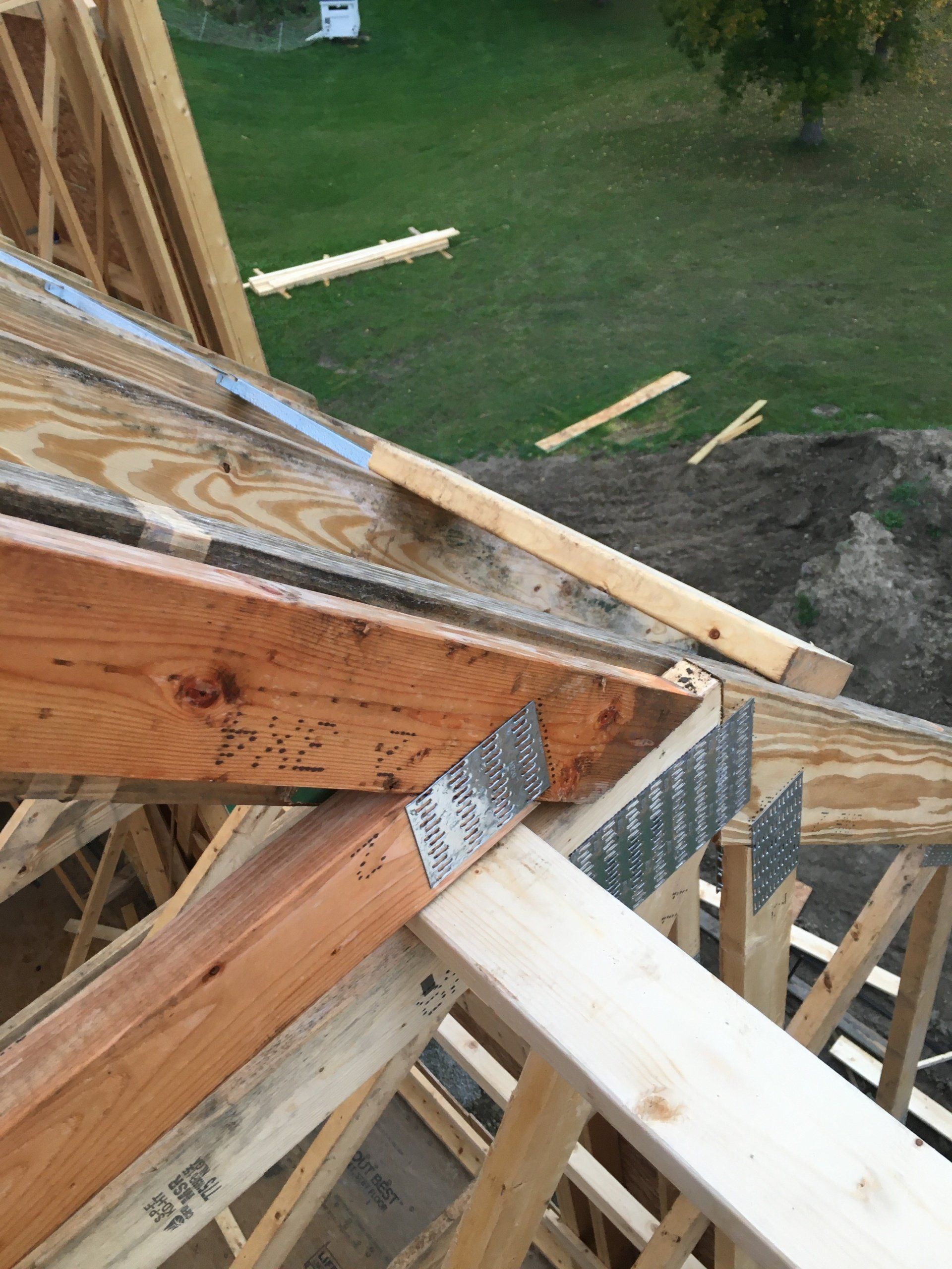 Wooden roof framing and trusses under construction overlooking a grassy yard