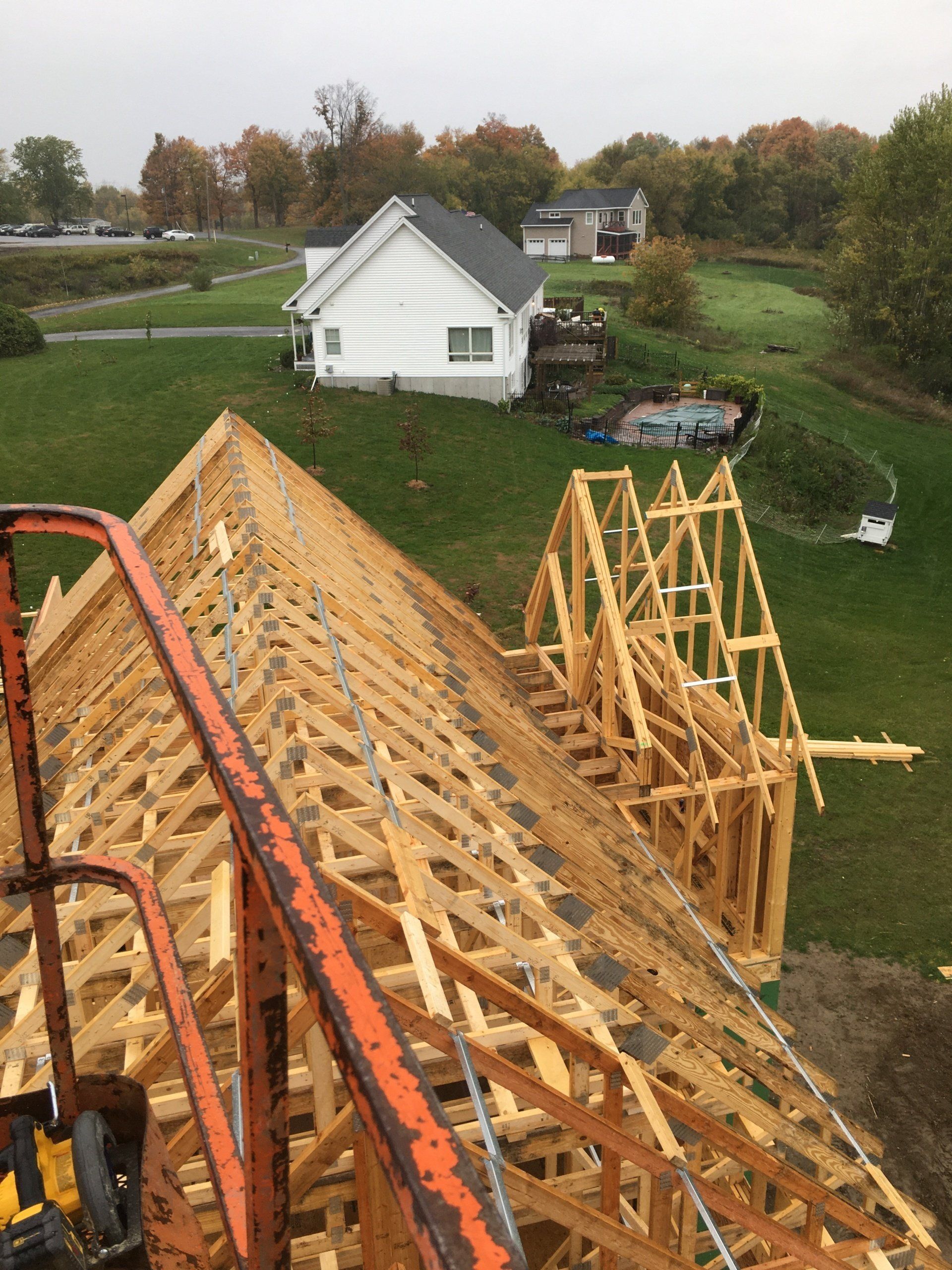 Partially framed roof under construction on a house, with a white shed and yard in the background