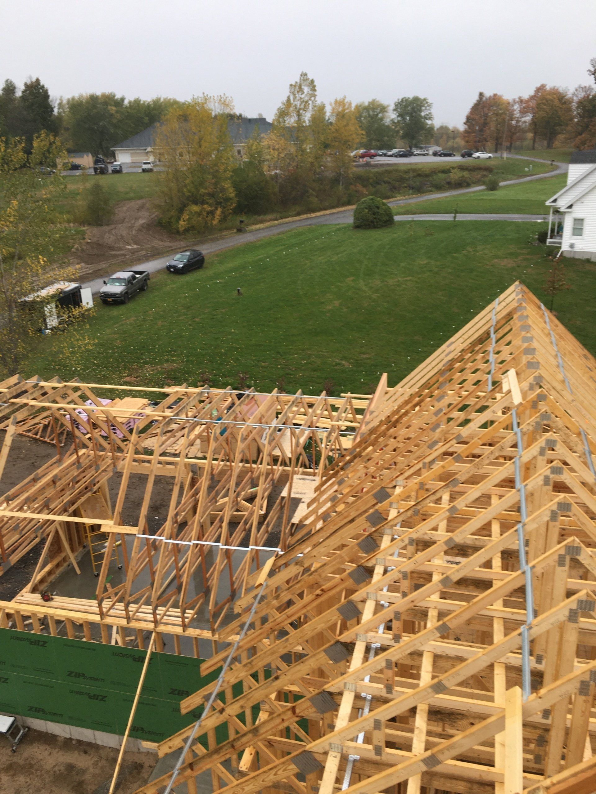 Roof trusses under construction on a house with a green lawn and autumn trees nearby