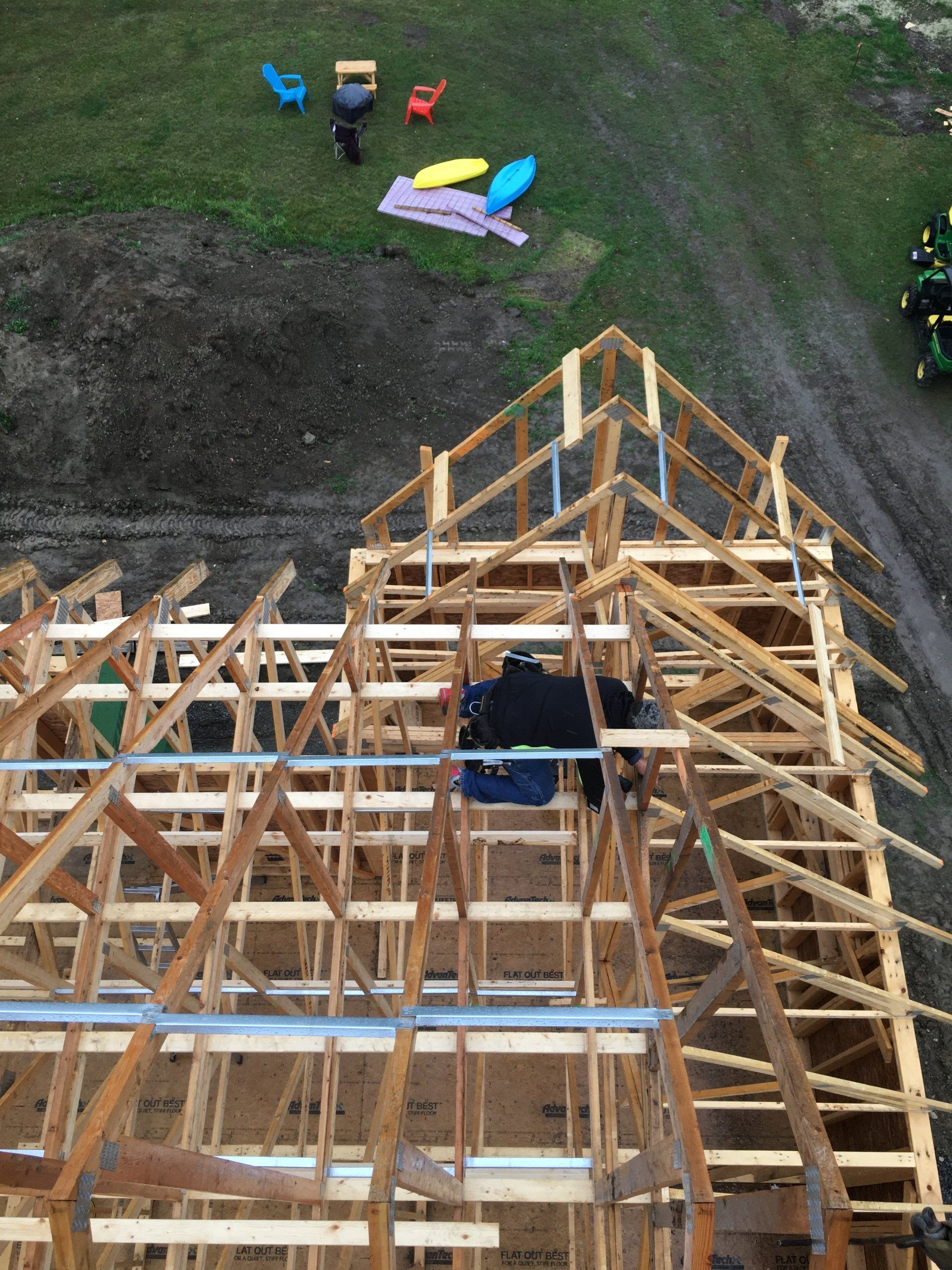 Overhead view of a wooden roof frame under construction with a few chairs on the grass nearby