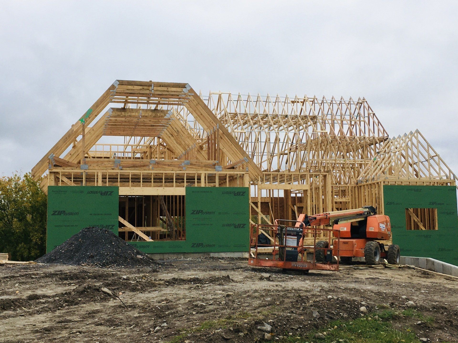 House under construction with wooden framing, green sheathing, and an orange excavator in front