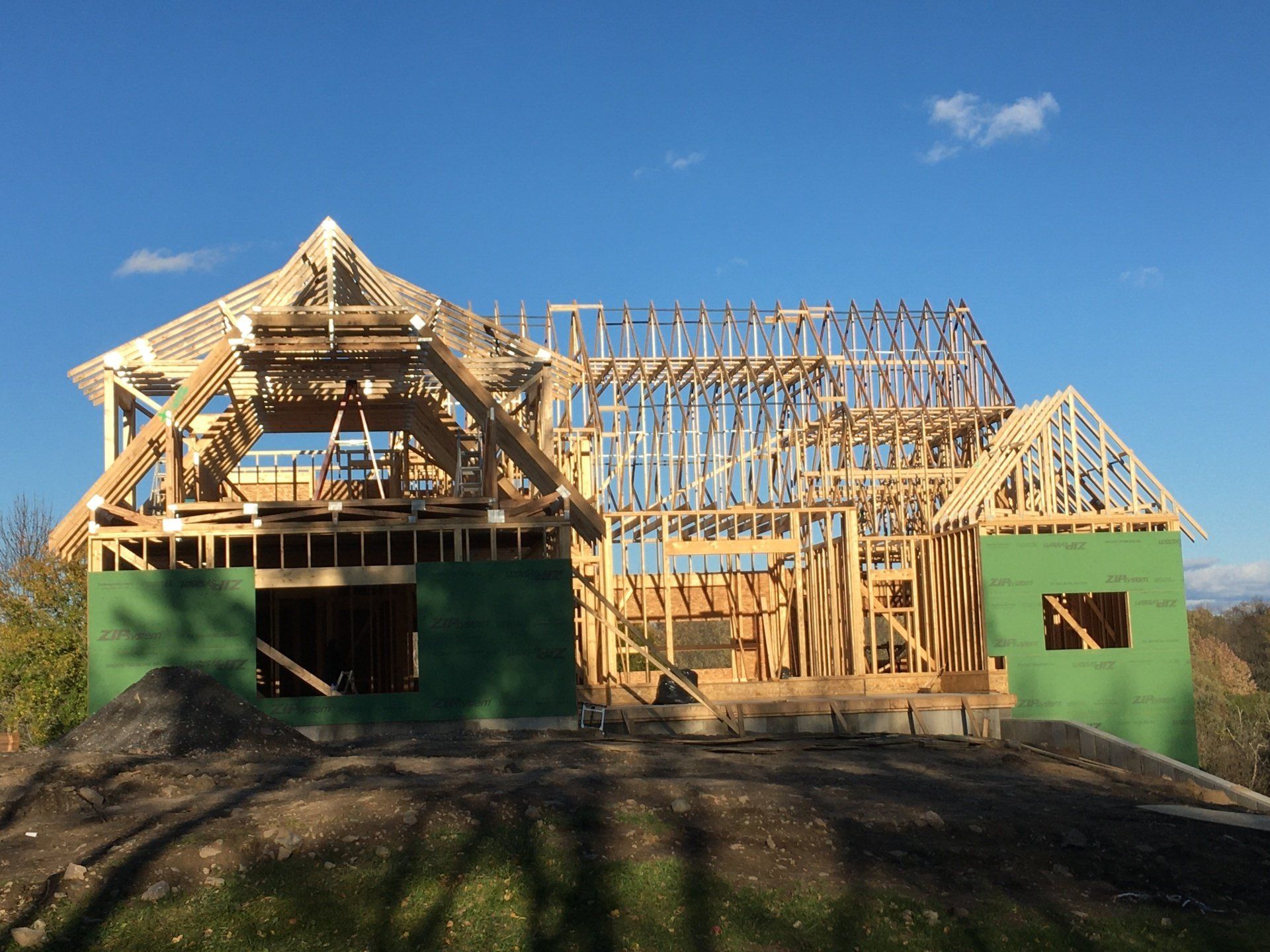 Partially built wooden house frame with green sheathing under a clear blue sky