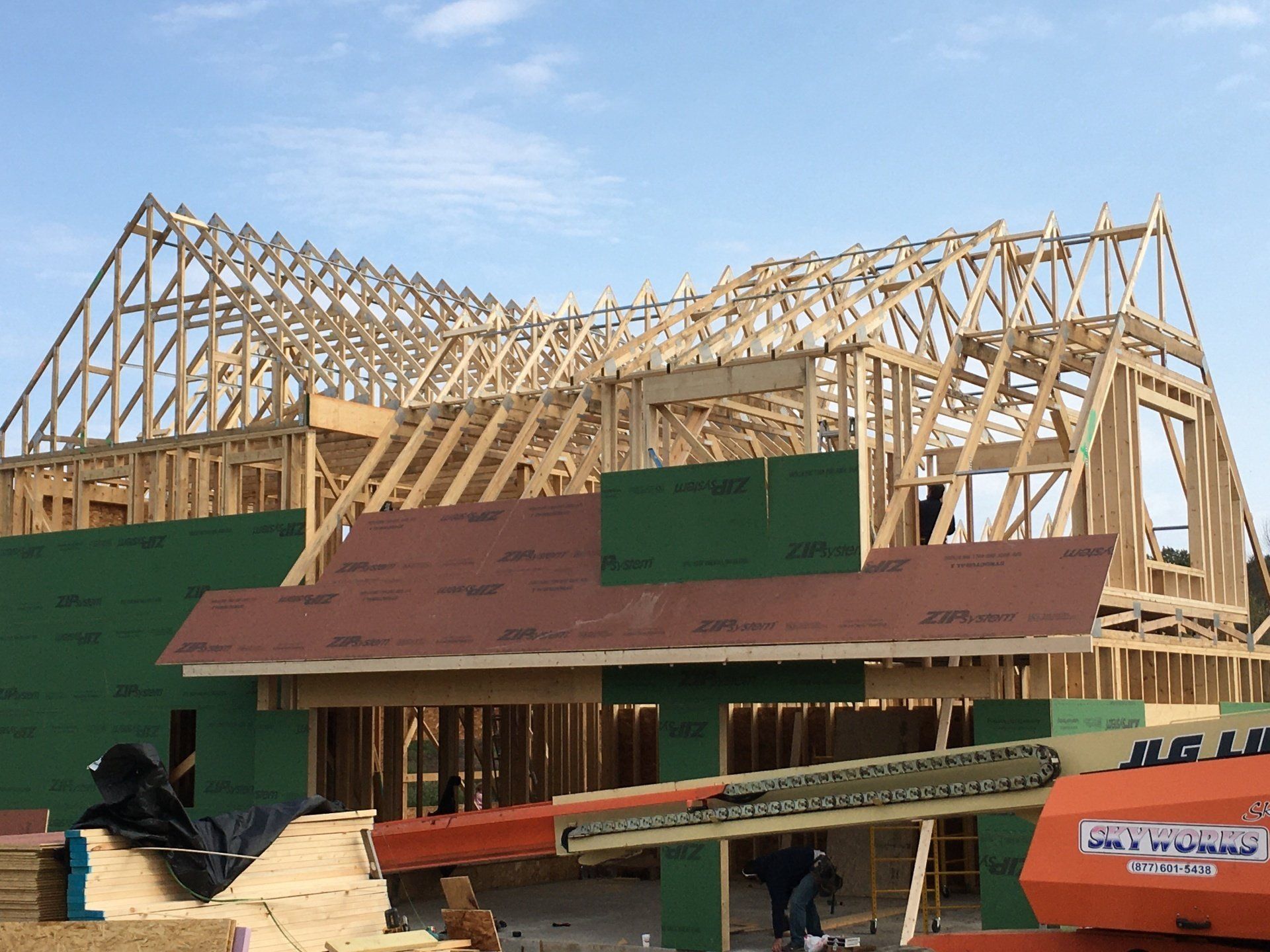 House under construction with wooden roof framing and green sheathing under a blue sky