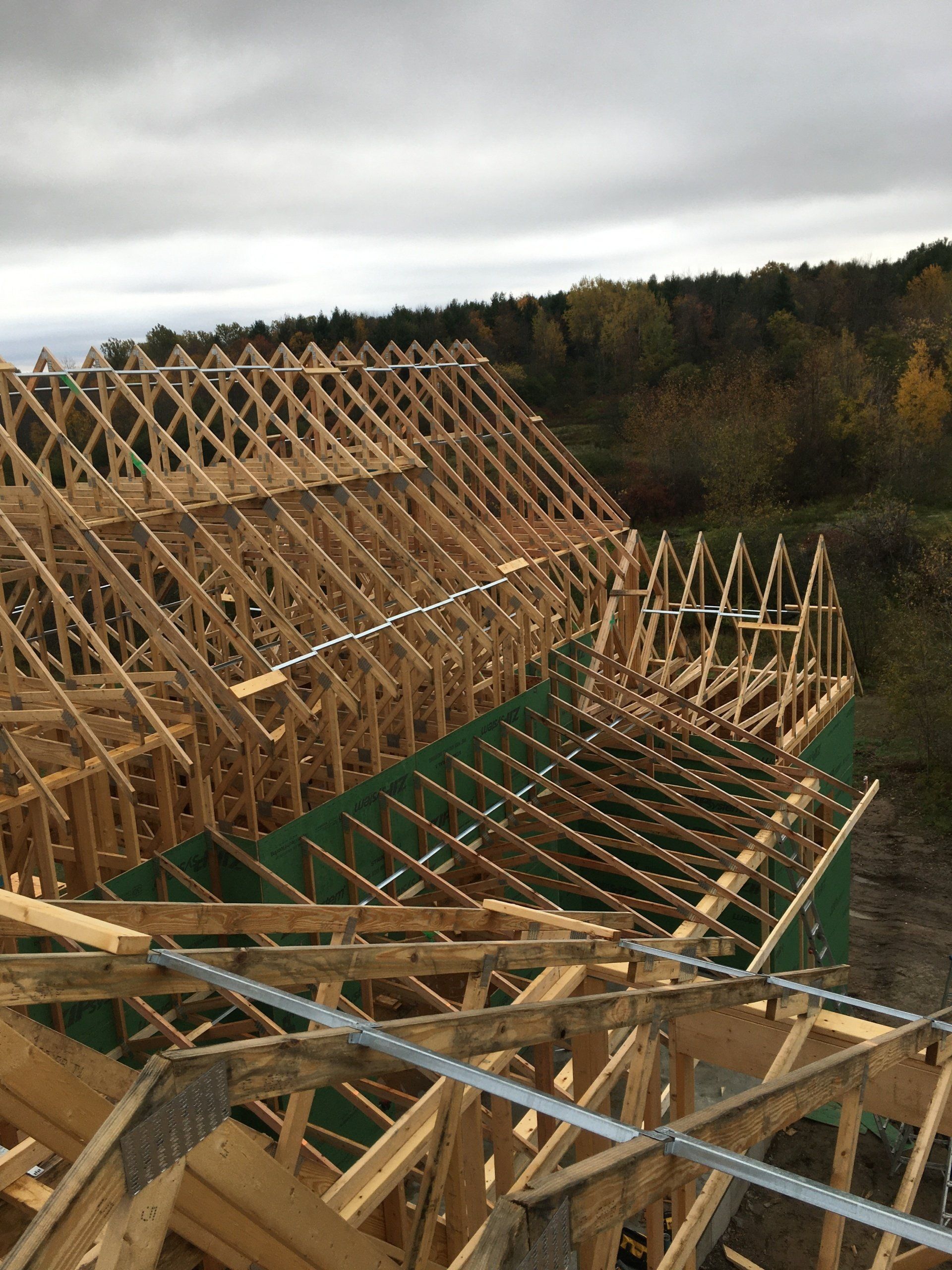 Wooden roof trusses under construction on a building site, with forest and cloudy sky in the background