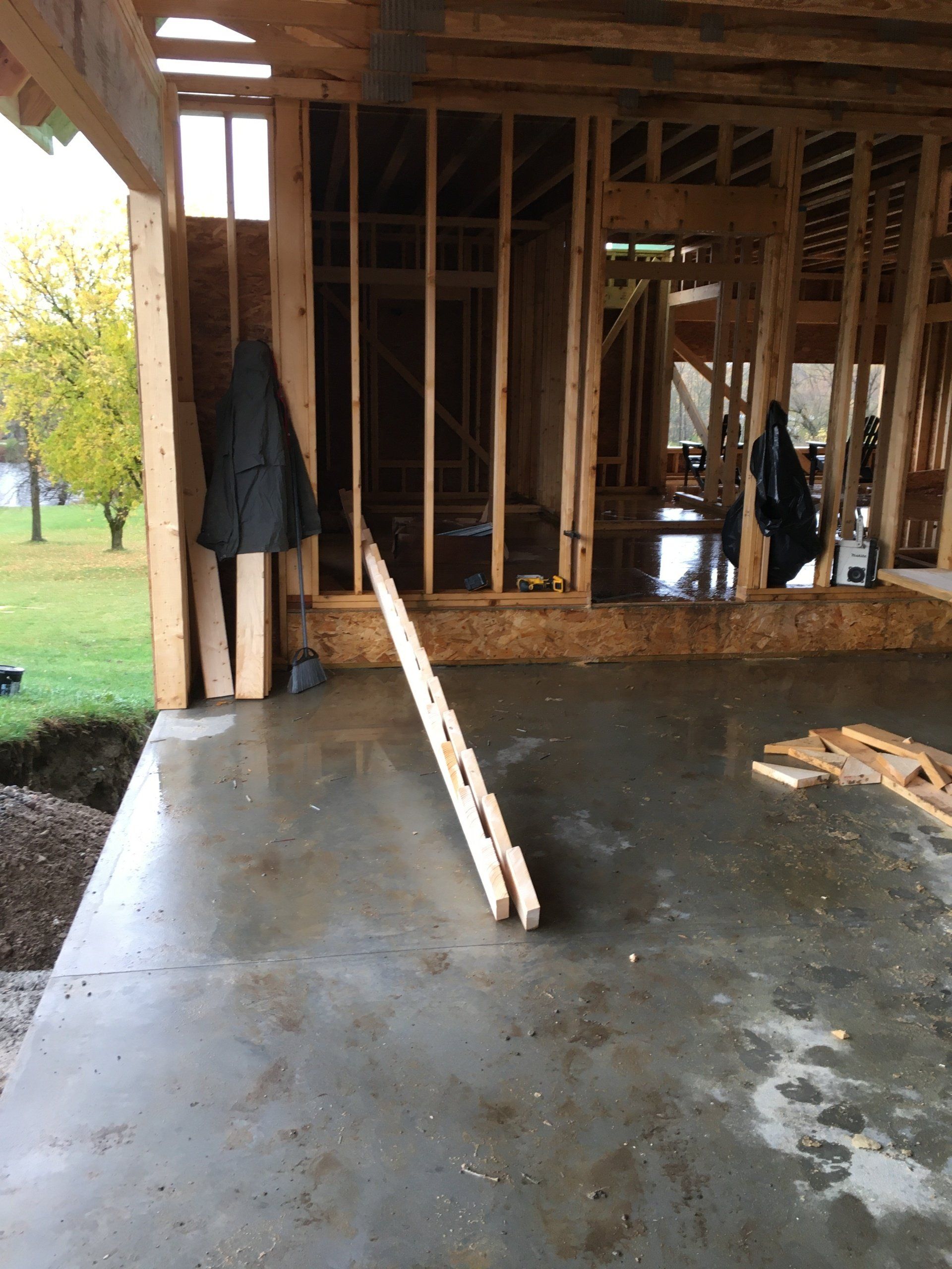 Unfinished house interior with exposed framing and a concrete floor; a board leans in the foreground.