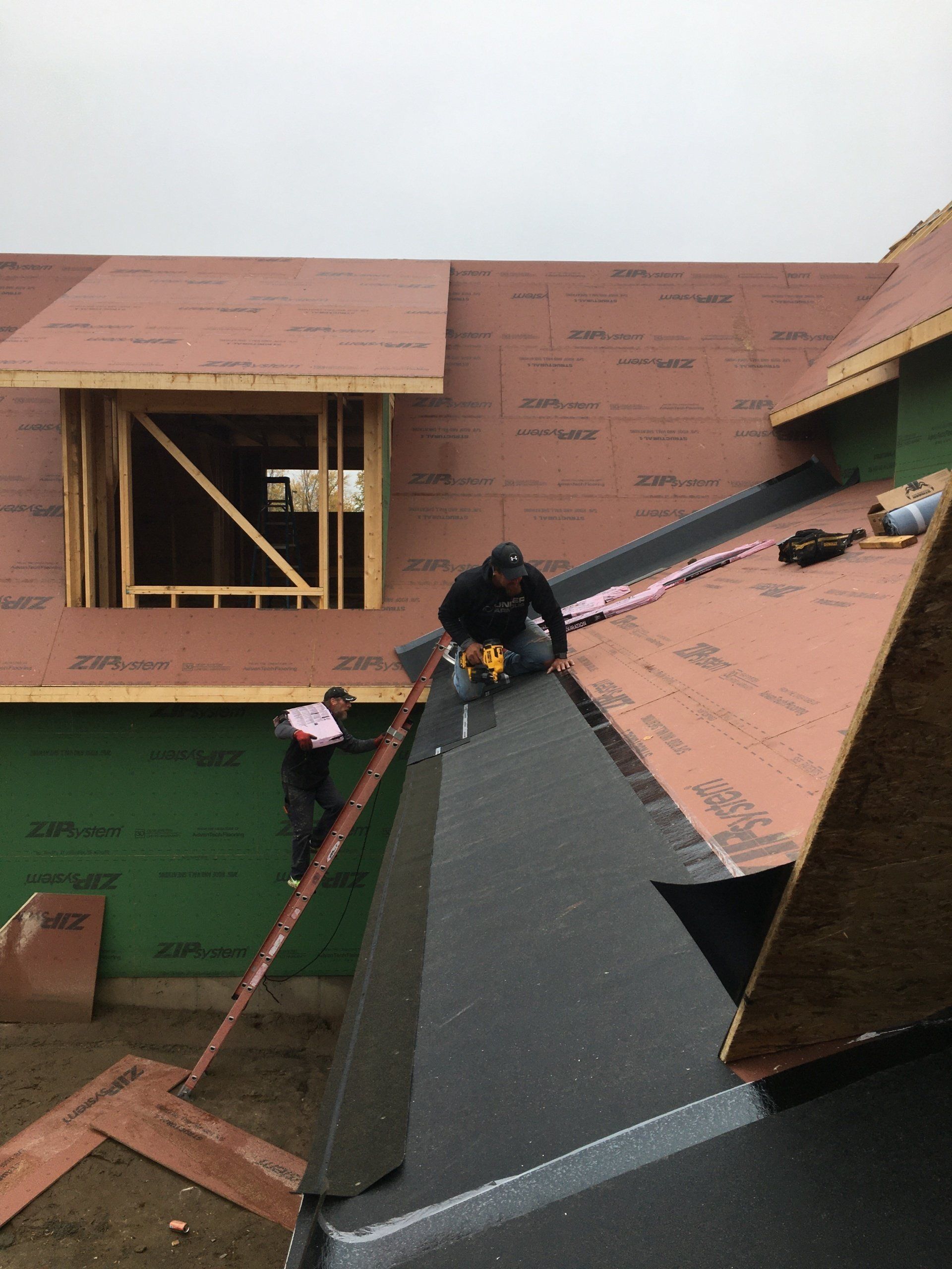 Workers installing black roofing on a house, with exposed plywood and shingles in progress.