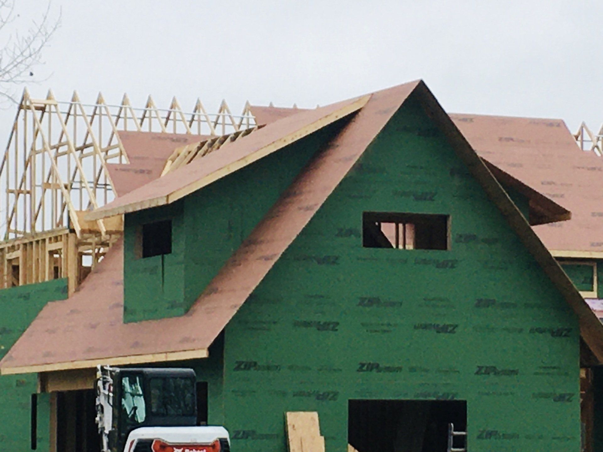 Partially built house wrapped in green house wrap with a red roof on a construction site