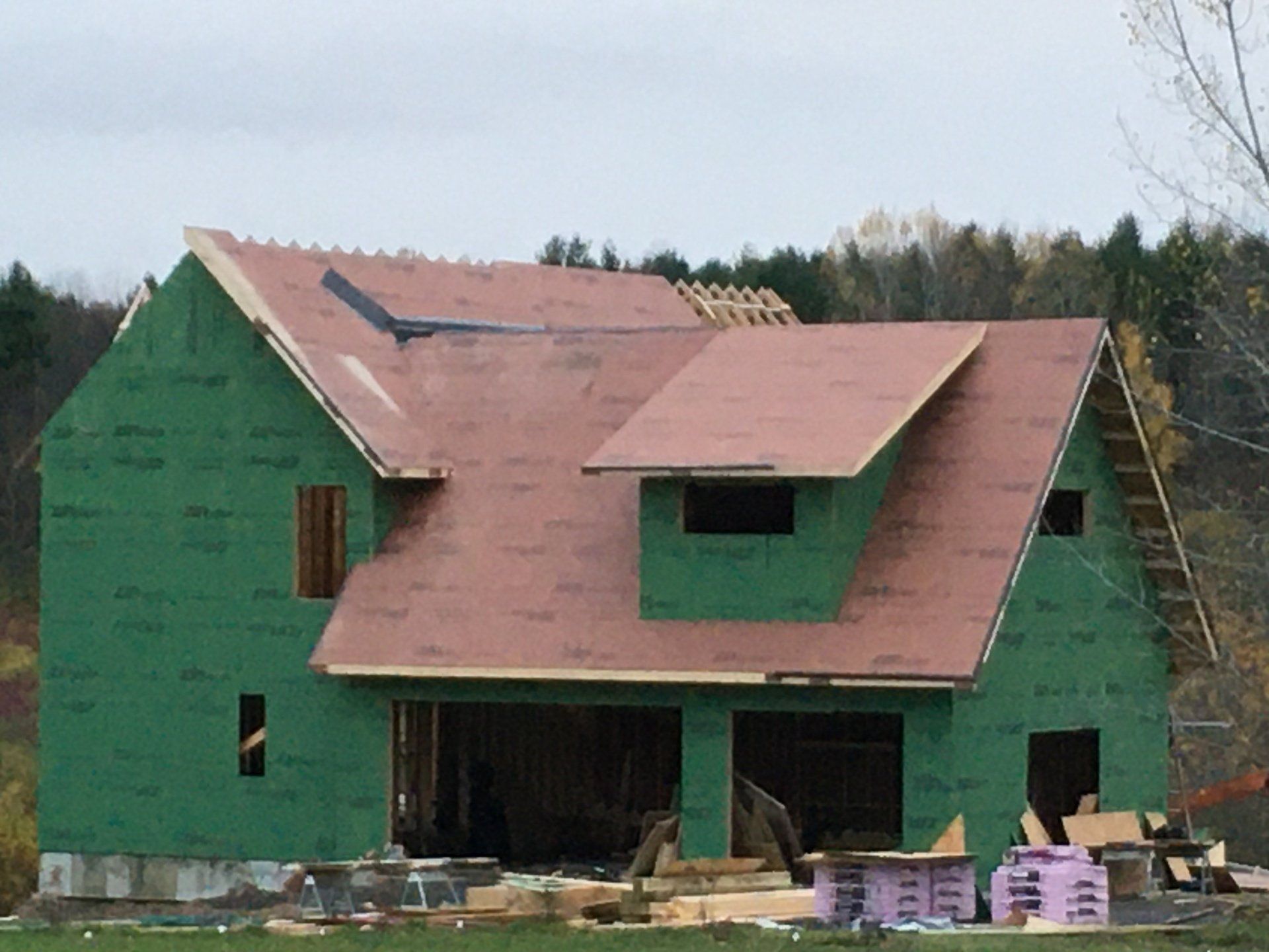 Green house under construction with pink roof sheathing and open windows.