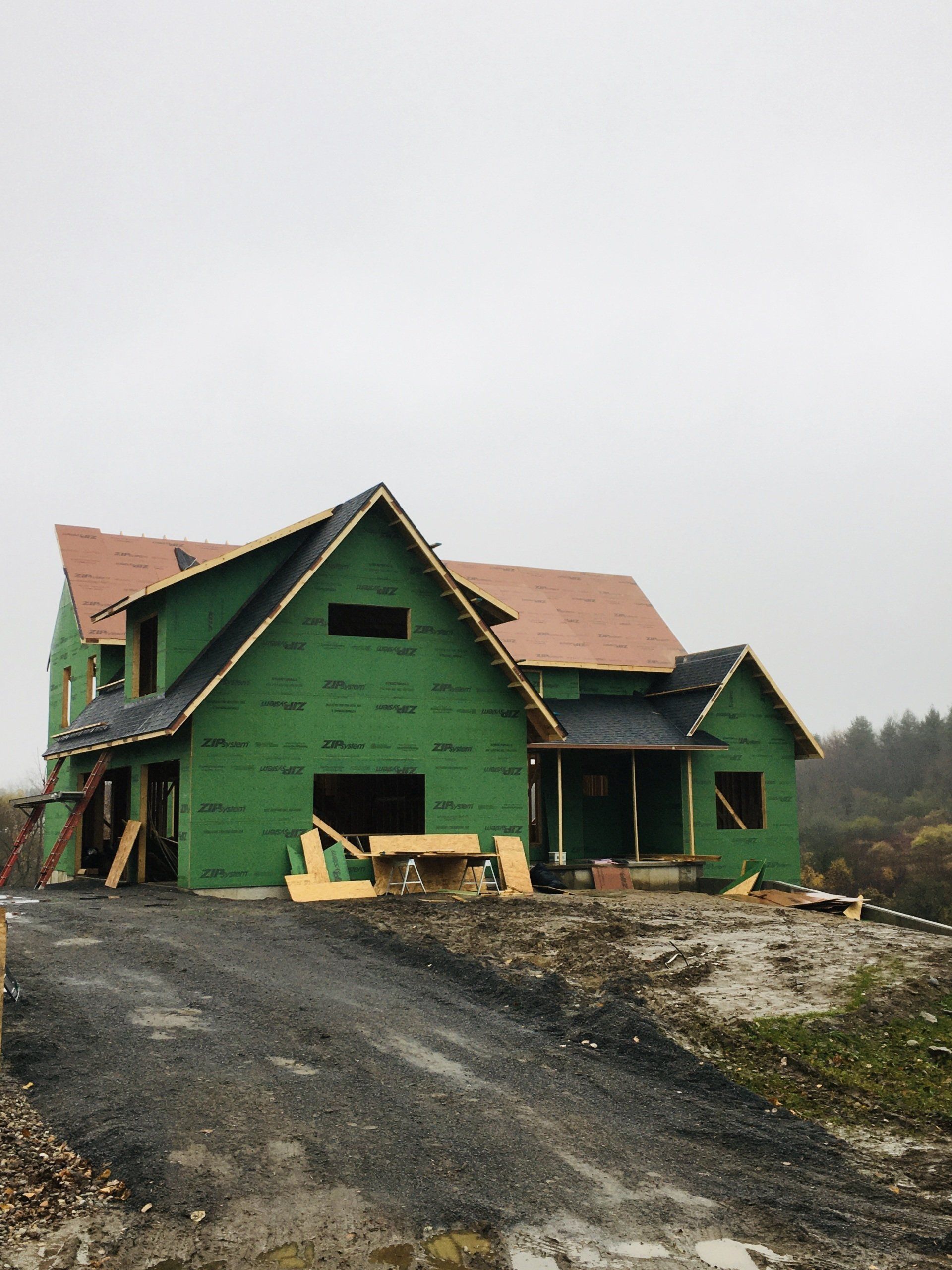 Partially built green house with tan roof on a gravel lot under an overcast sky