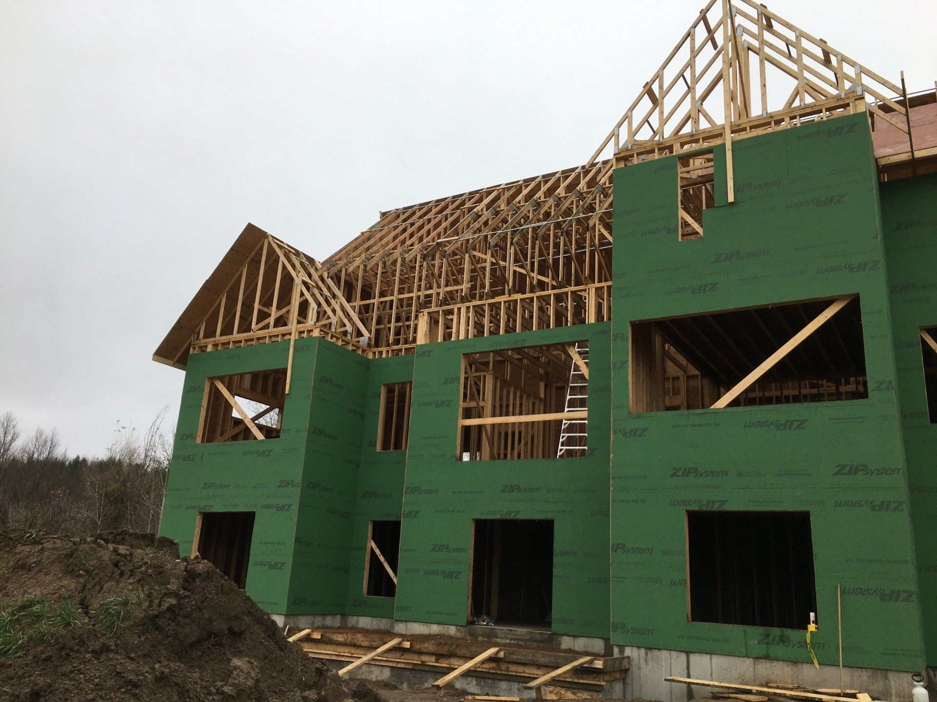 Partially built house with green sheathing and exposed wooden roof framing on a dirt lot