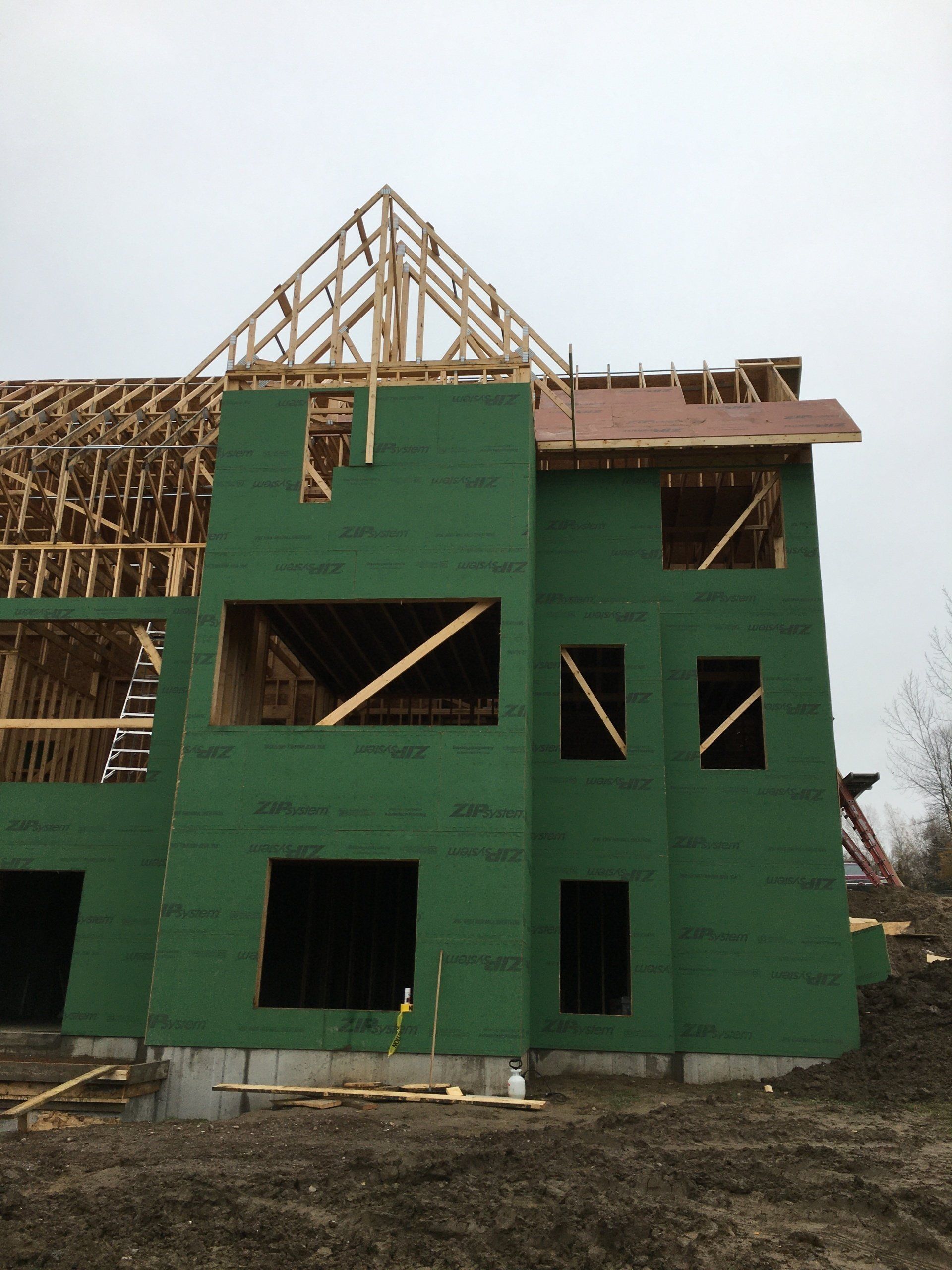 Green sheathed house under construction with exposed wood framing and unfinished roof.