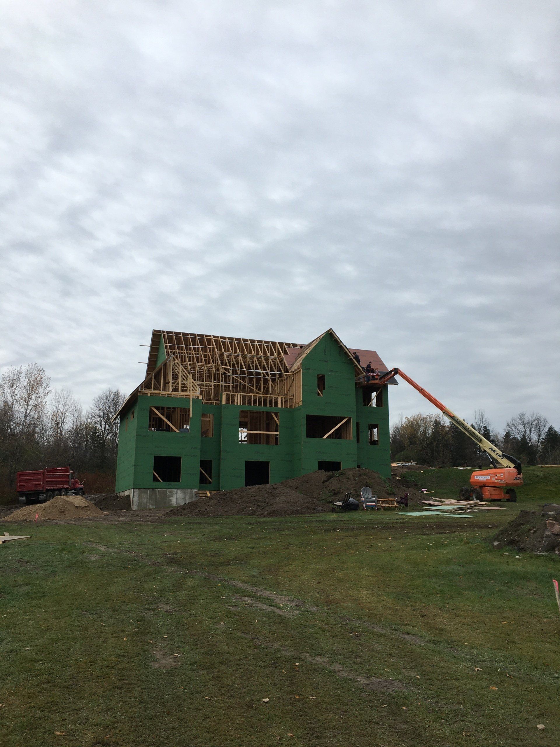 Partially demolished green house with a collapsed roof and construction machinery in a grassy field under cloudy skies