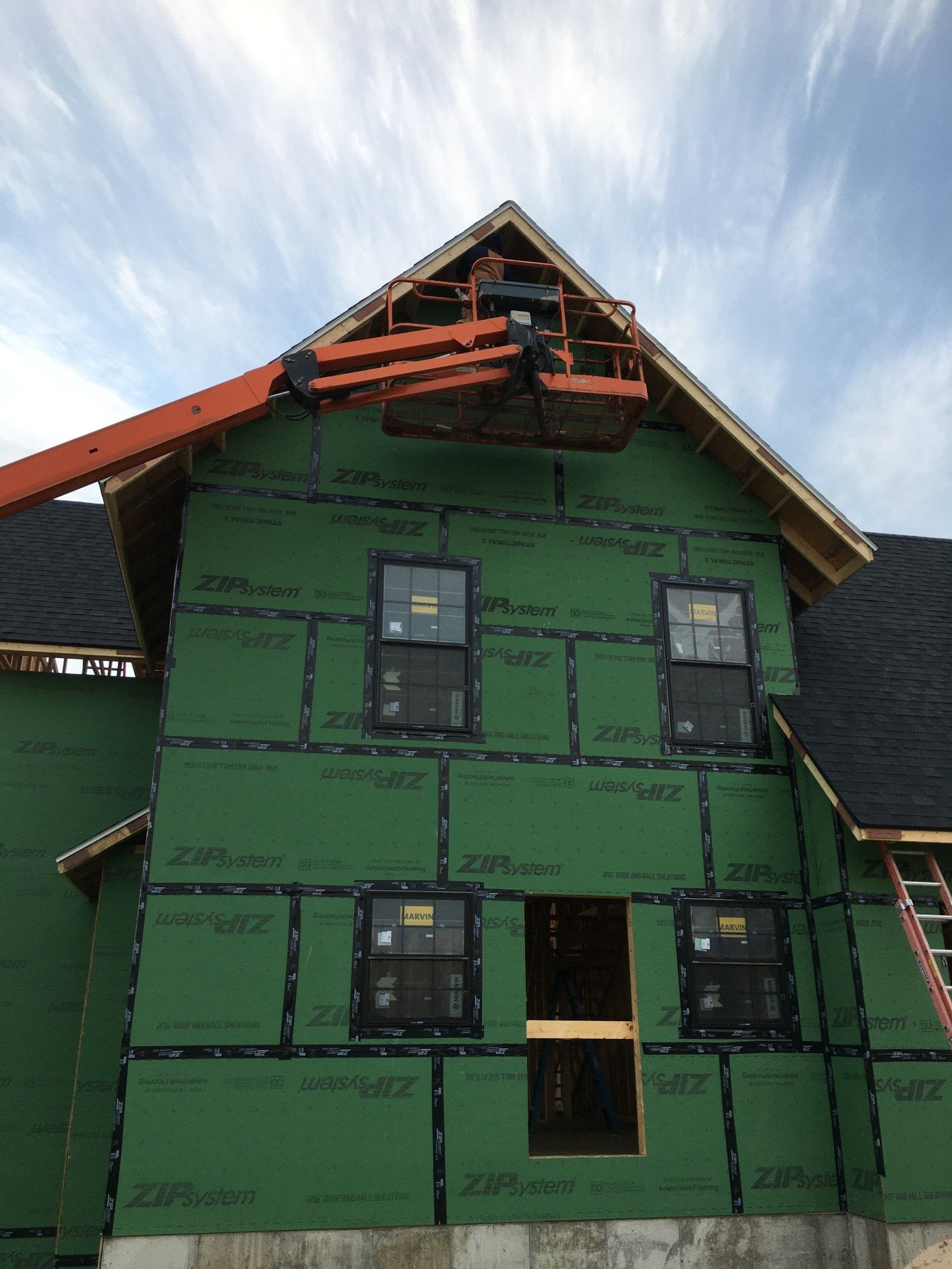 Partially finished green house with black-trimmed windows and exposed roof framing under a blue sky