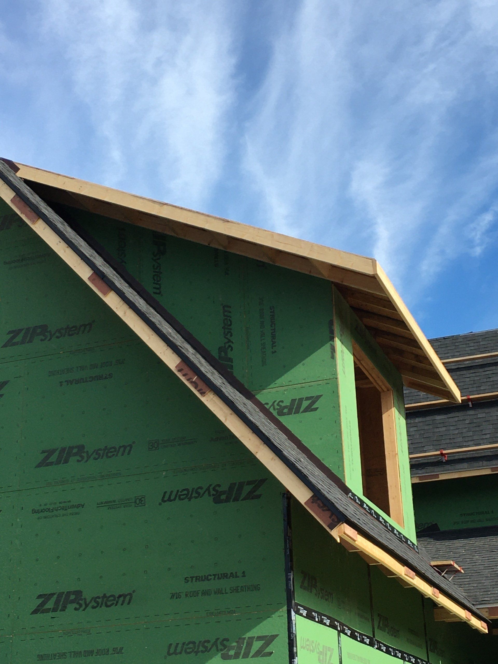 Green house exterior under construction with ZIP System sheathing and roof framing against a blue sky