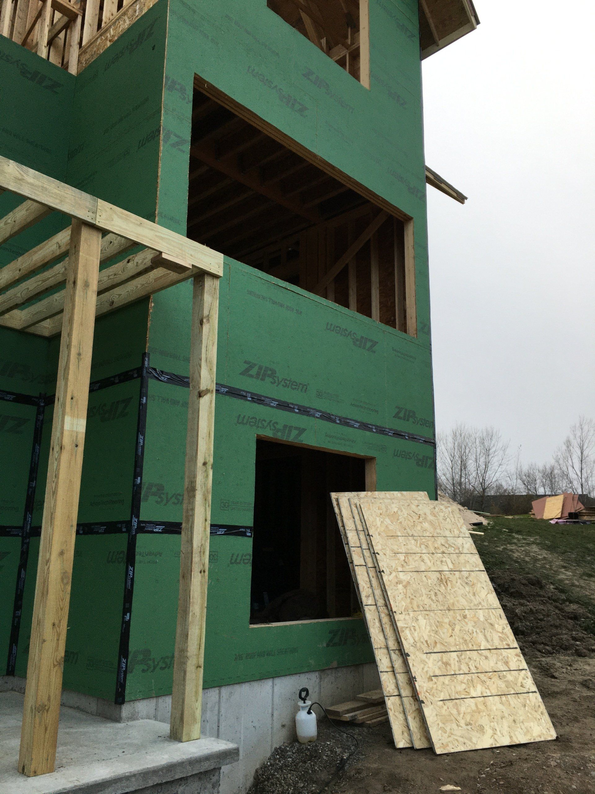 Green building under construction with plywood boards leaning against an open doorway.