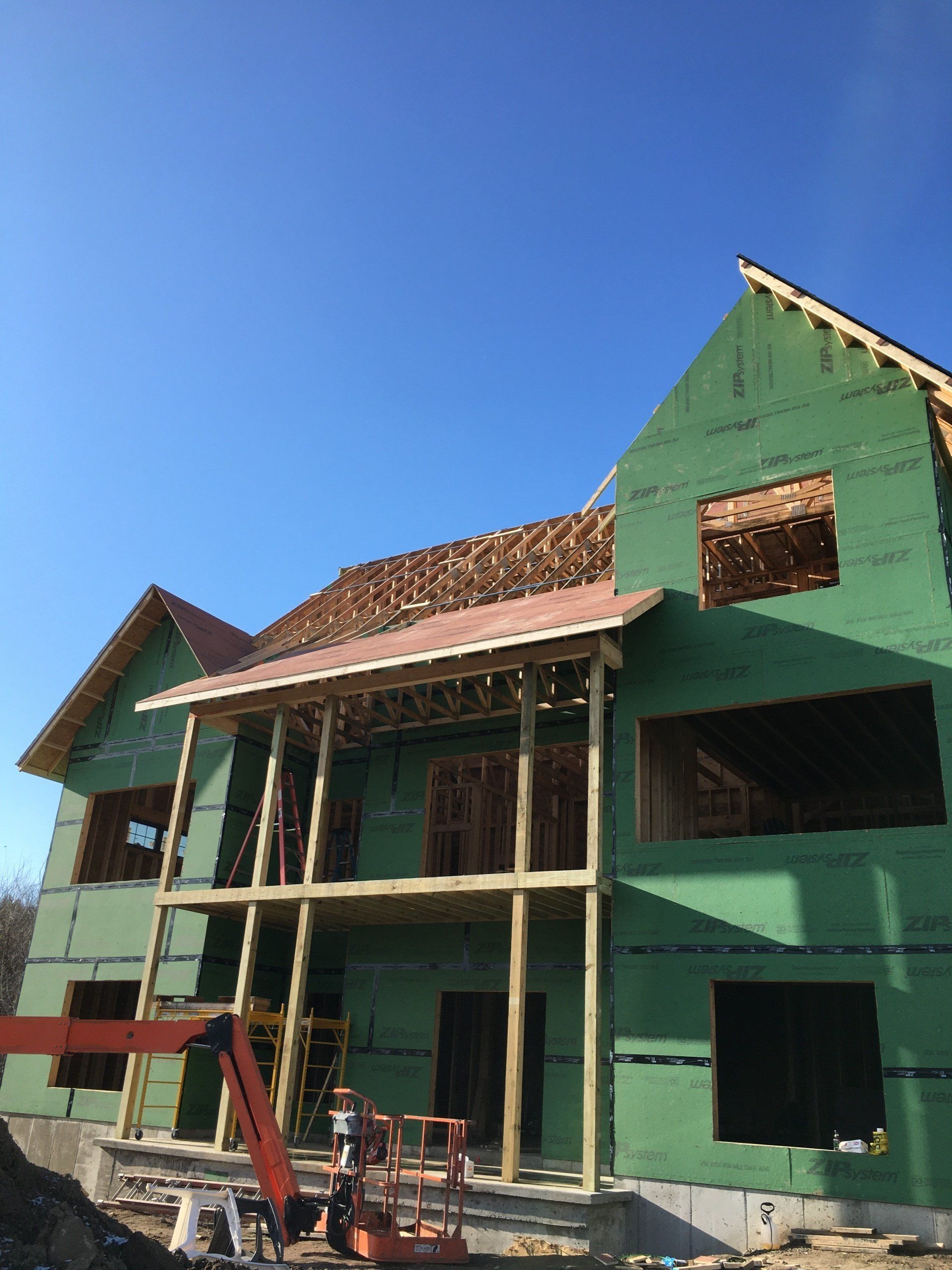 Partially built green house with exposed framing and workers under a clear blue sky