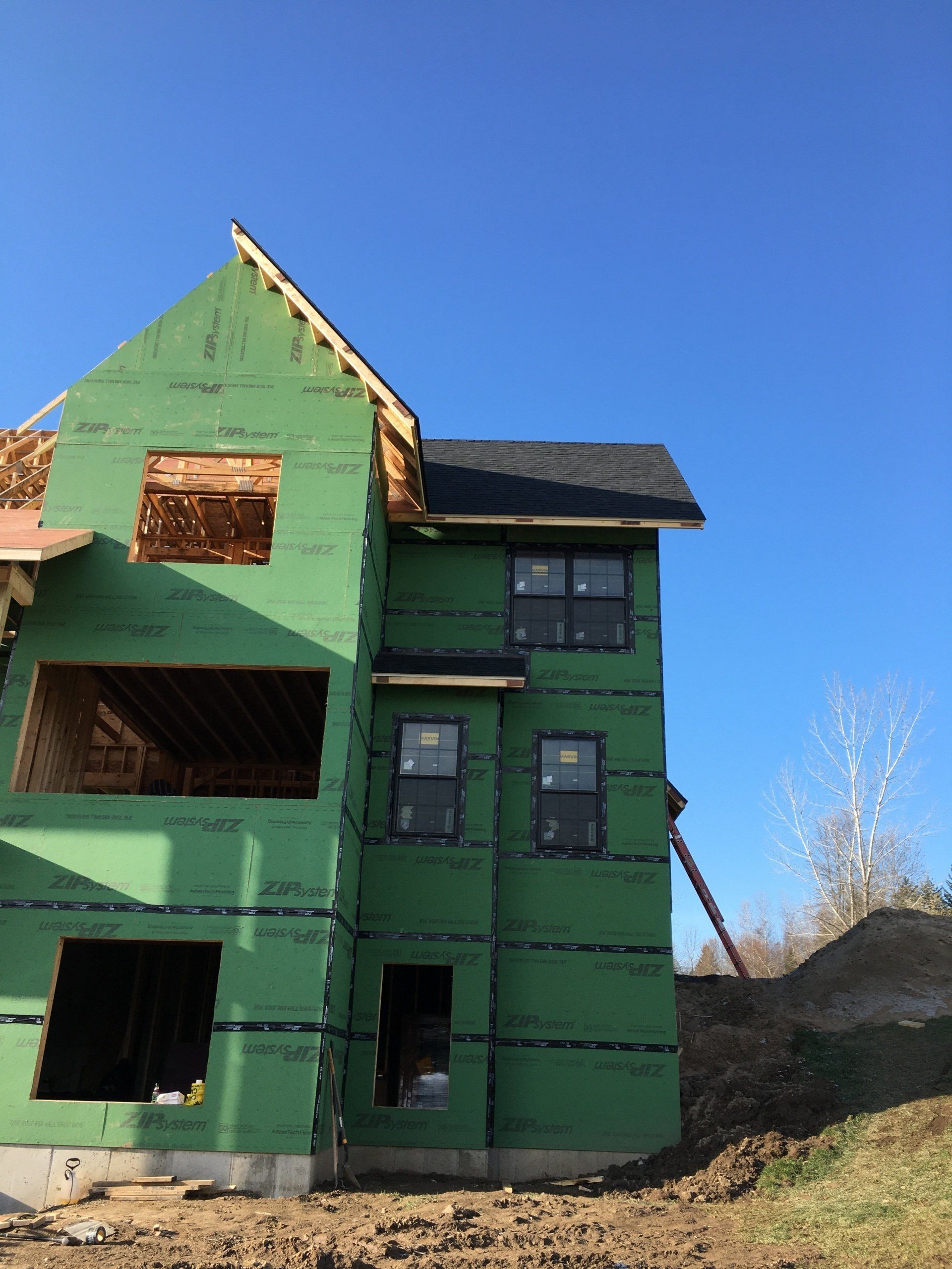 Green two-story house under construction with exposed wood framing and a blue sky backdrop