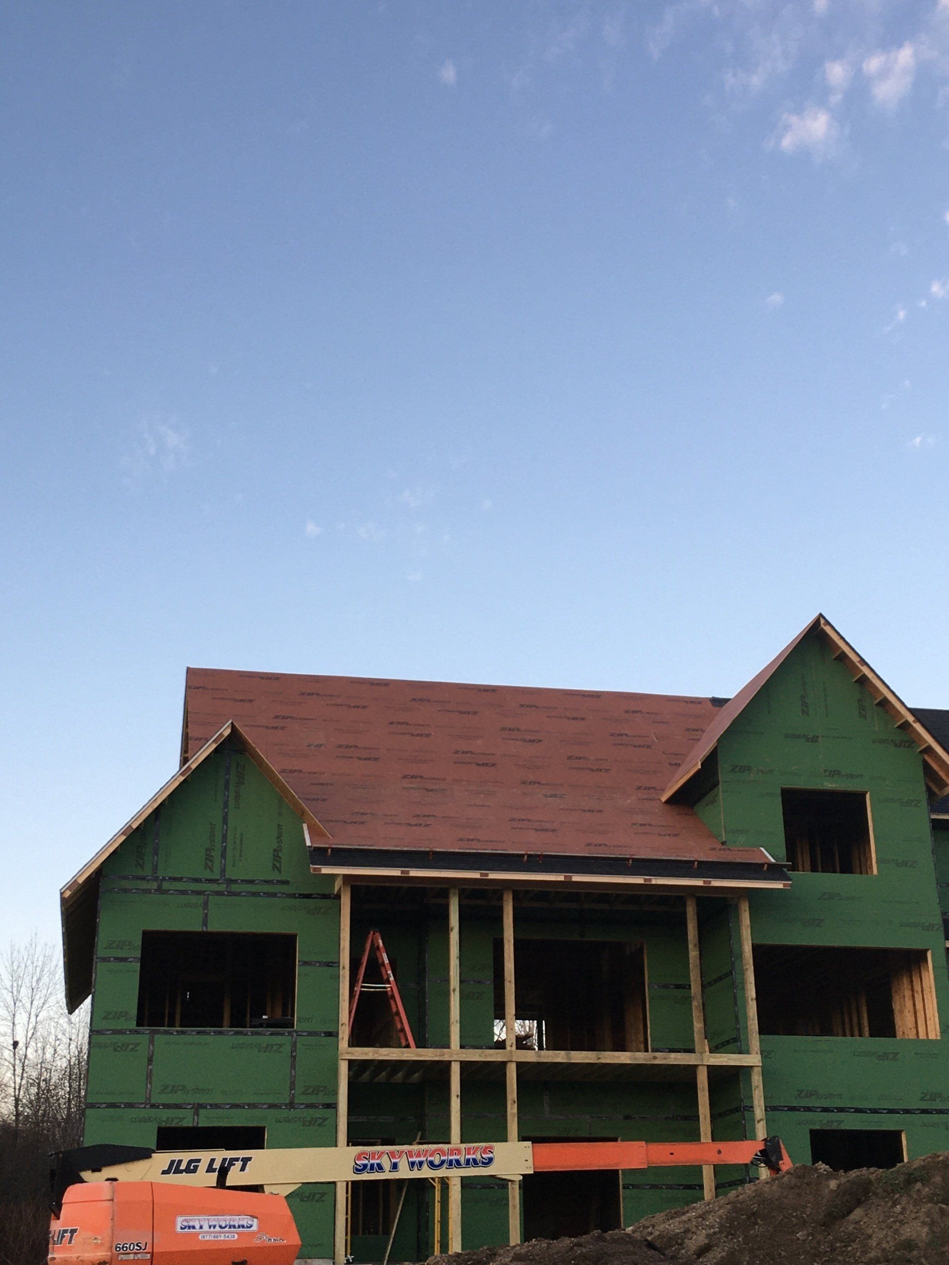 Green house under construction with a red roof and exposed framing under a blue sky