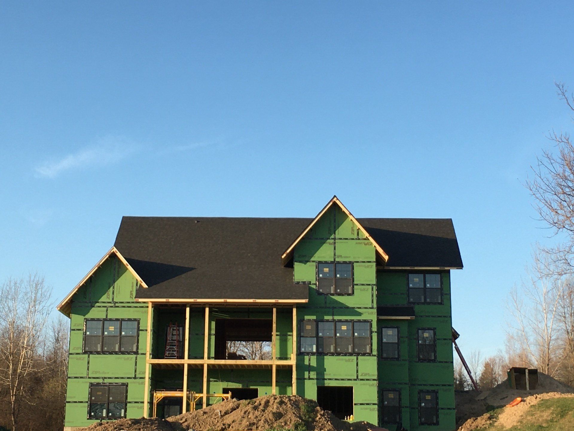 Green house under construction with dark roof, front porches, and blue sky background