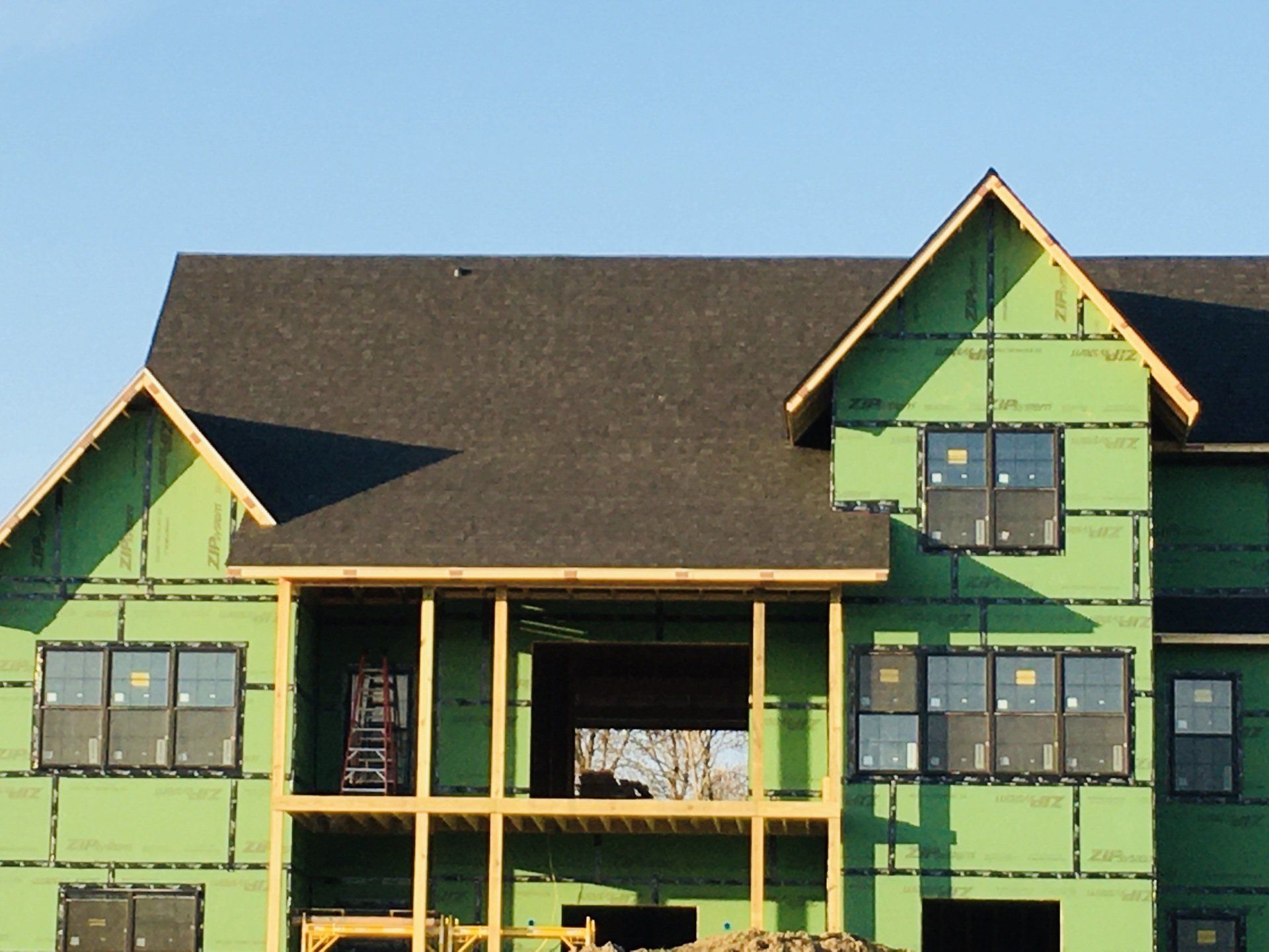 Green house under construction with dark roof and exposed framing against a blue sky