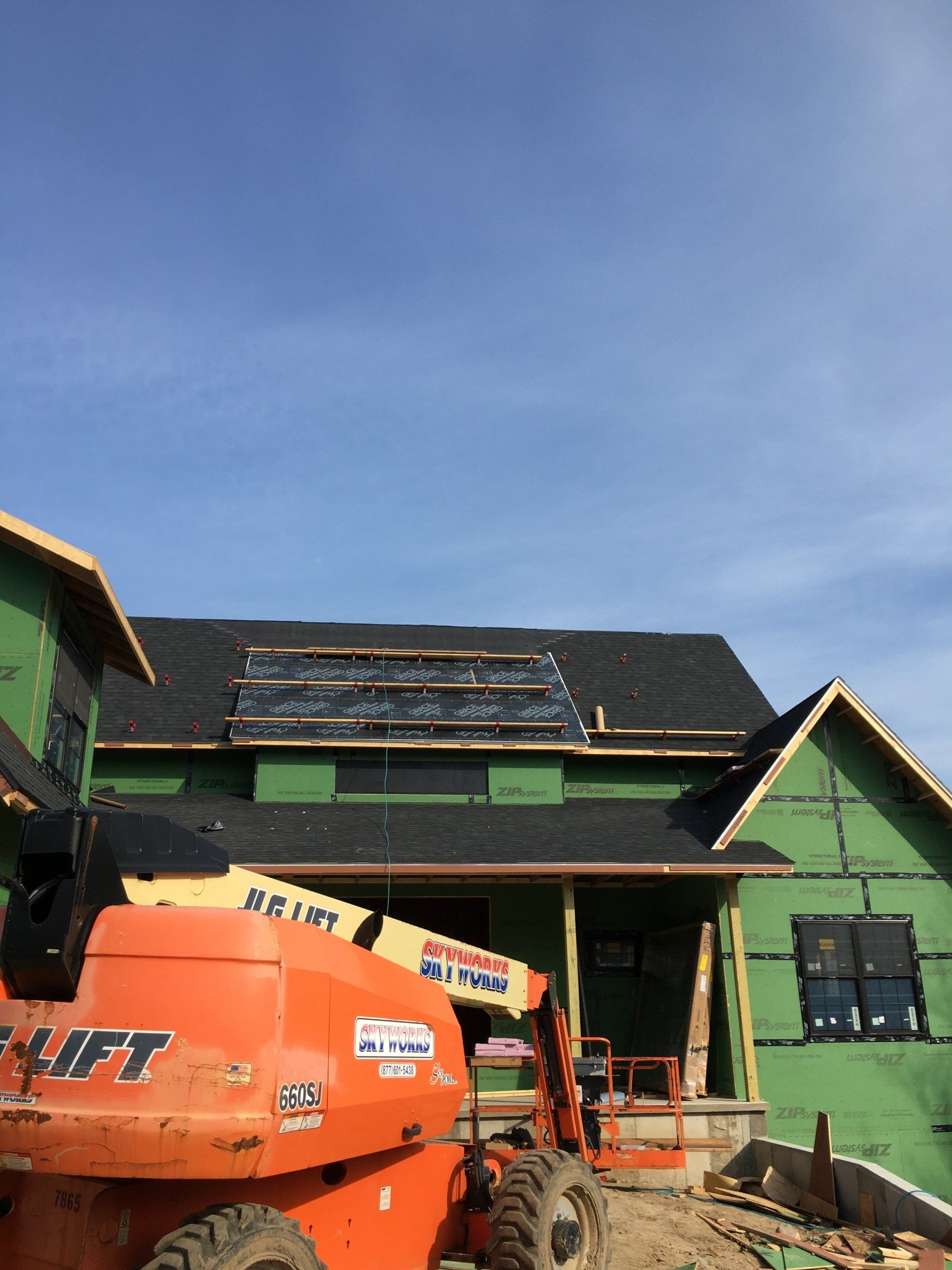 Orange construction lift in front of a green house under roof repair against a blue sky