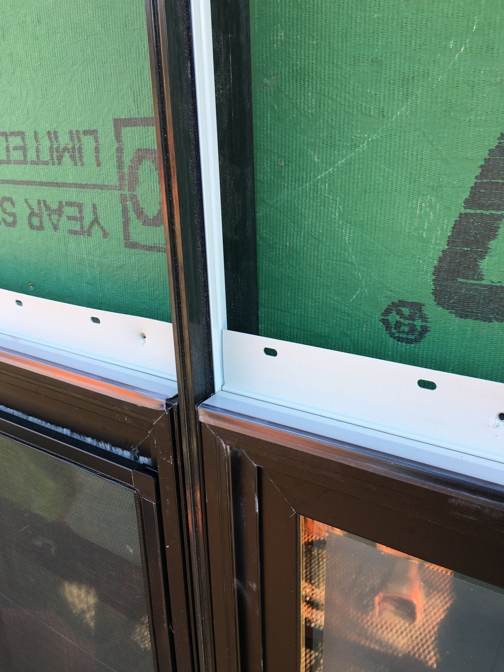 Close-up of a window frame with green protective sheeting outside and reflections on the glass.