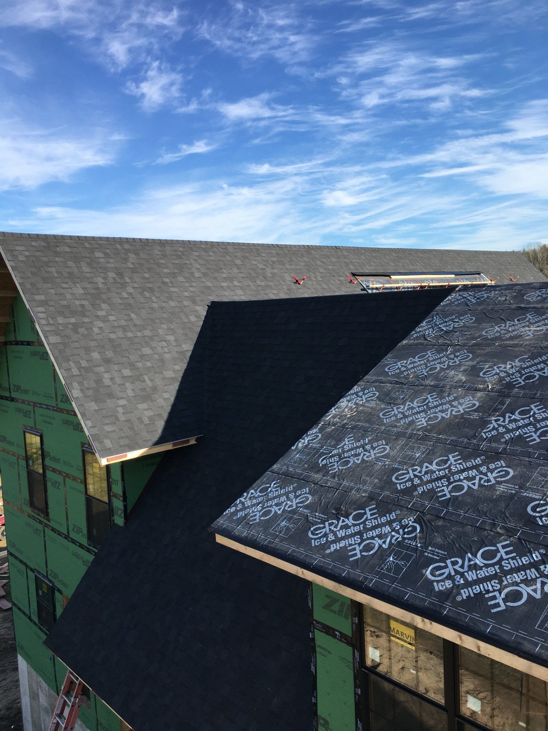 Rooftop with dark shingles and a black awning under a bright blue sky with wispy clouds