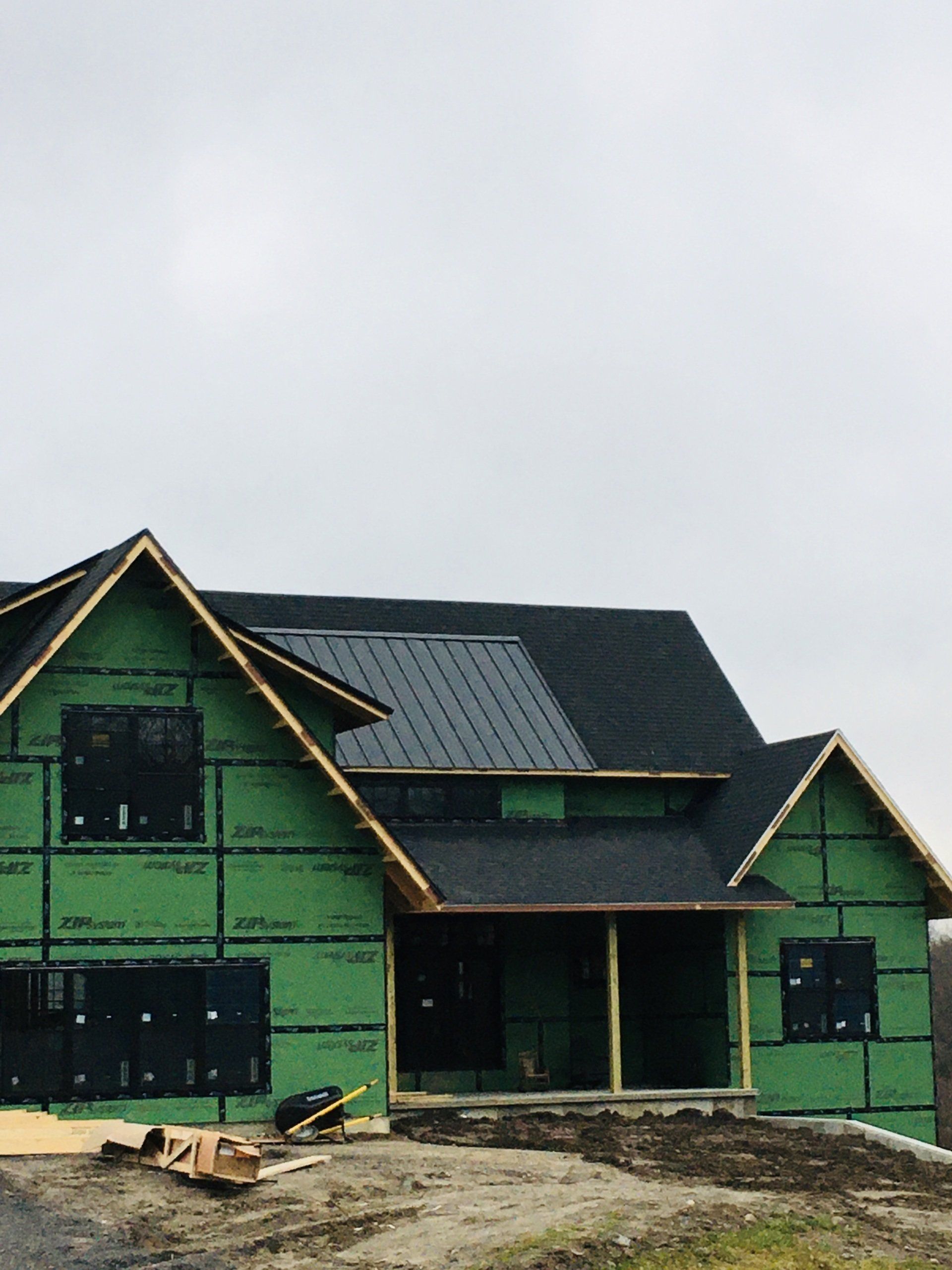 Partially built green house with black roof and exposed framing under a cloudy sky