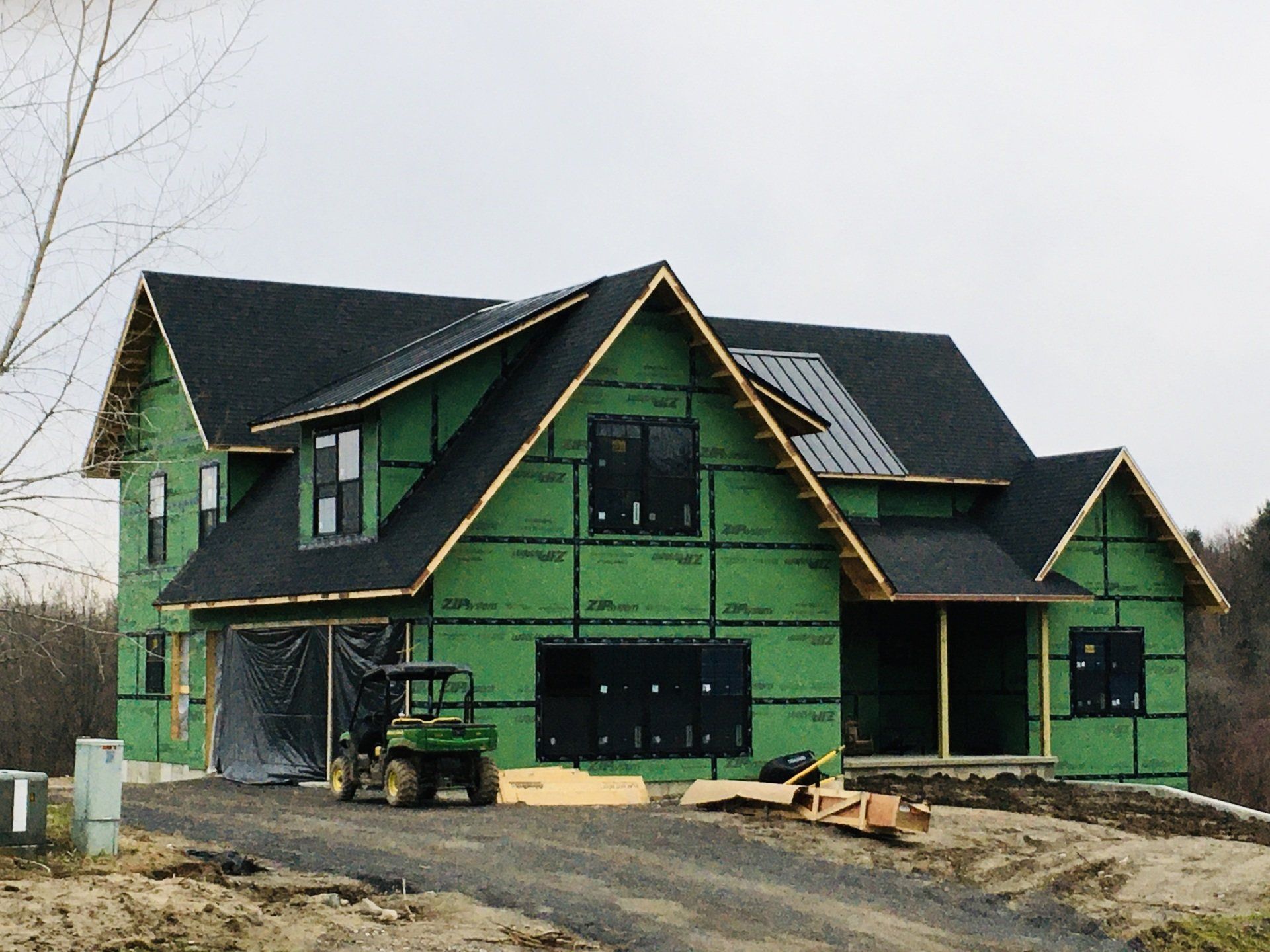 Partially built green house with dark roof and exposed framing on a muddy construction site