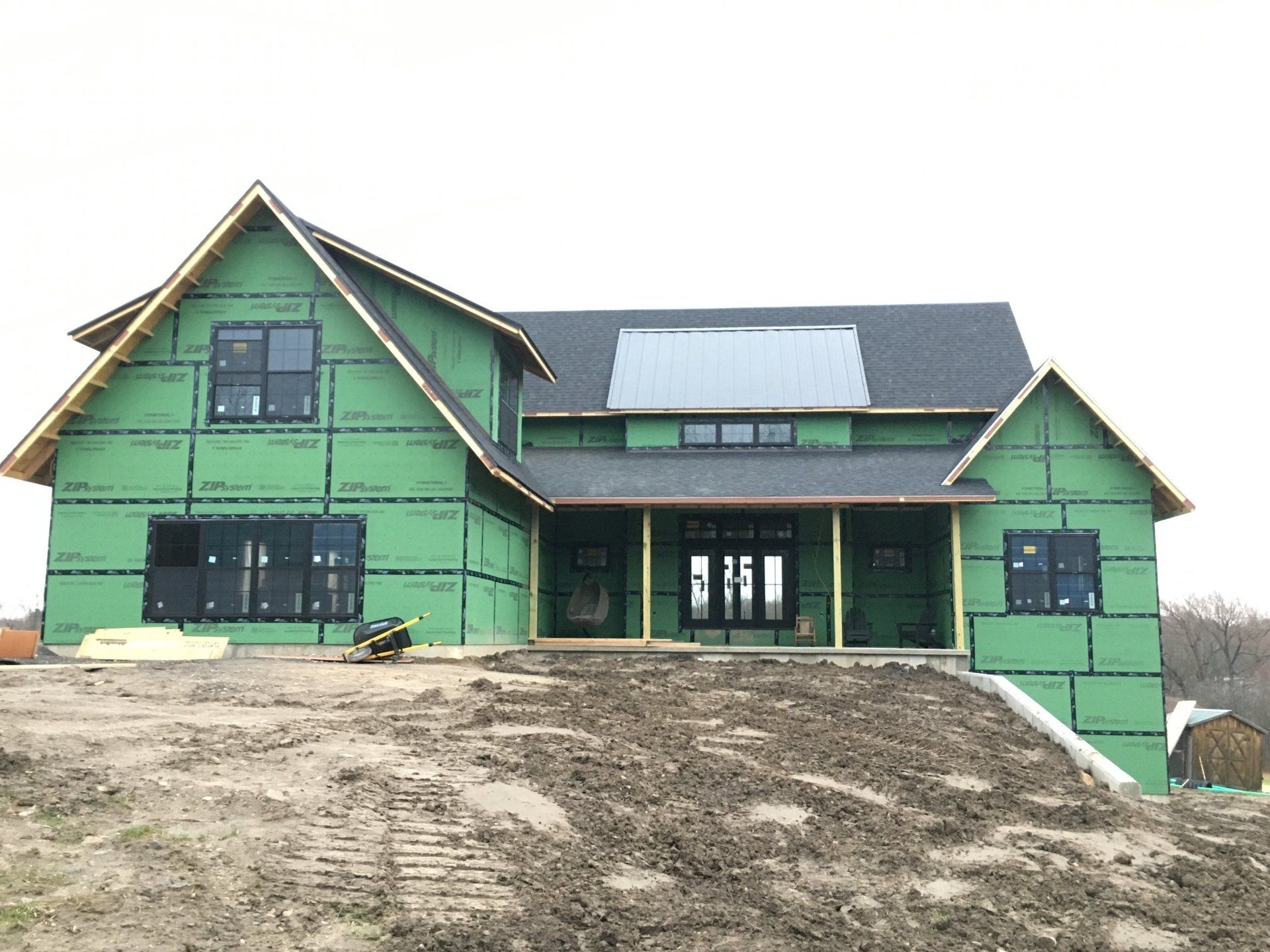 Green house under construction on a dirt lot, with dark trim and a covered front porch.