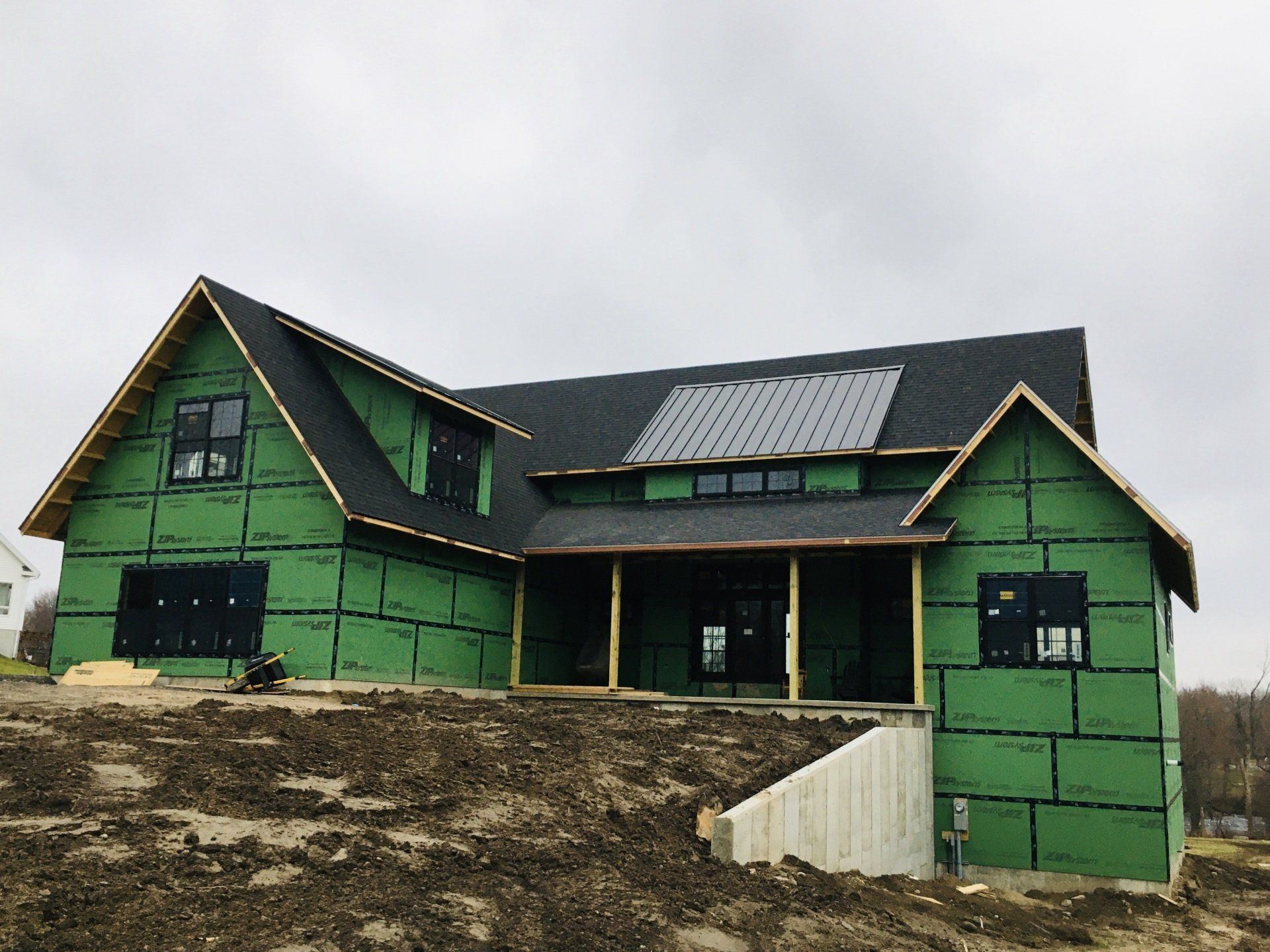 Green house under construction with black roof and unfinished dirt front yard
