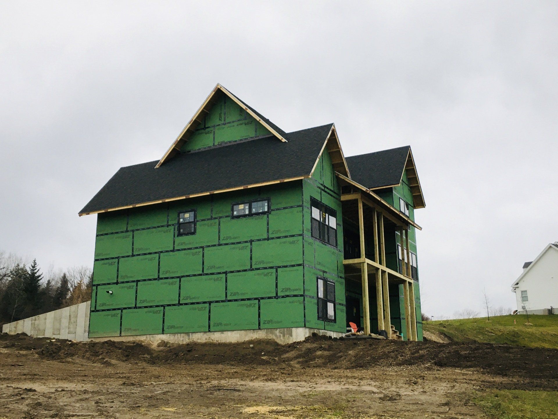Green house under construction on a dirt lot under an overcast sky