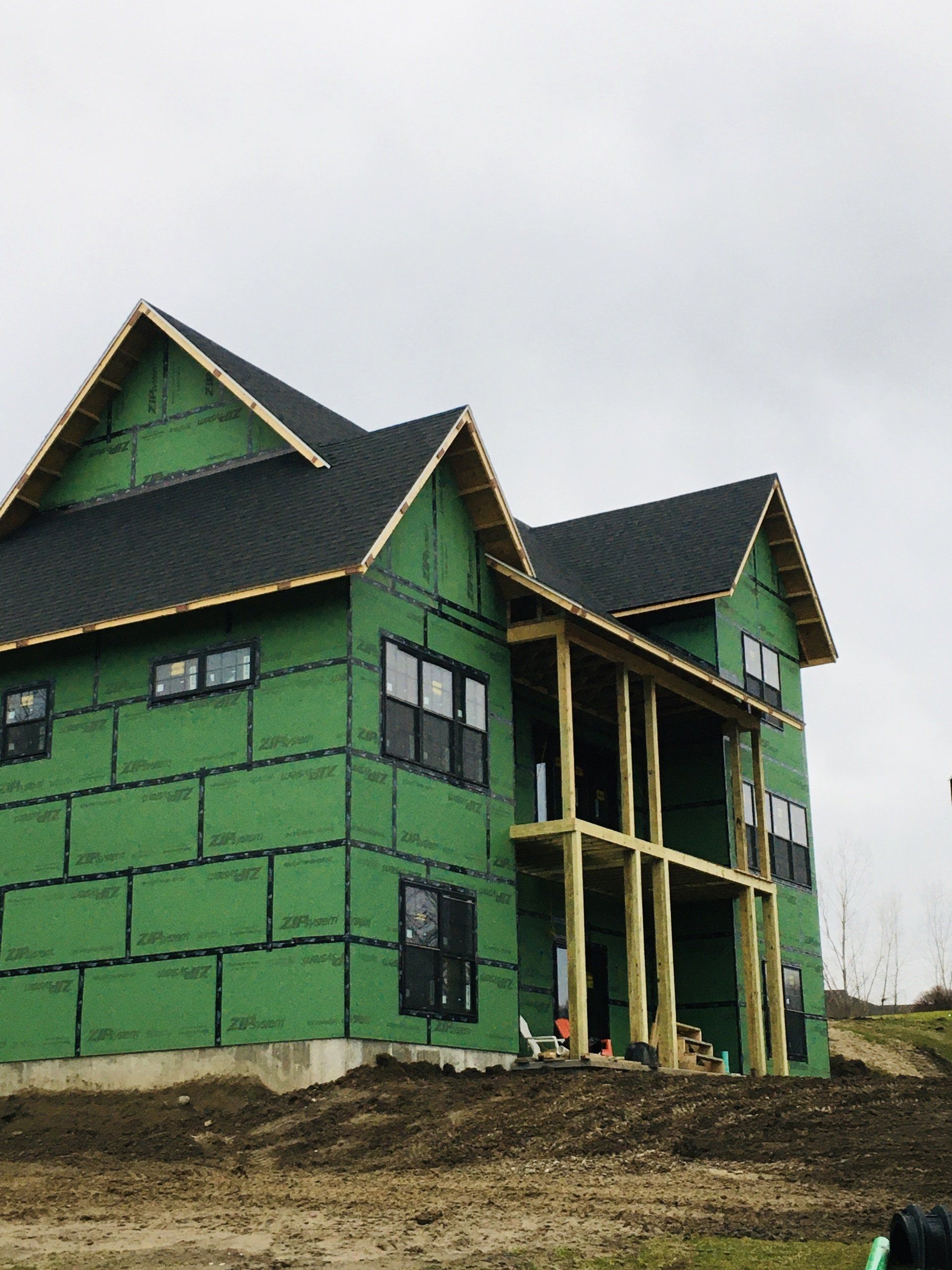 Partially built green house with dark roof and unfinished wooden framing on a dirt lot