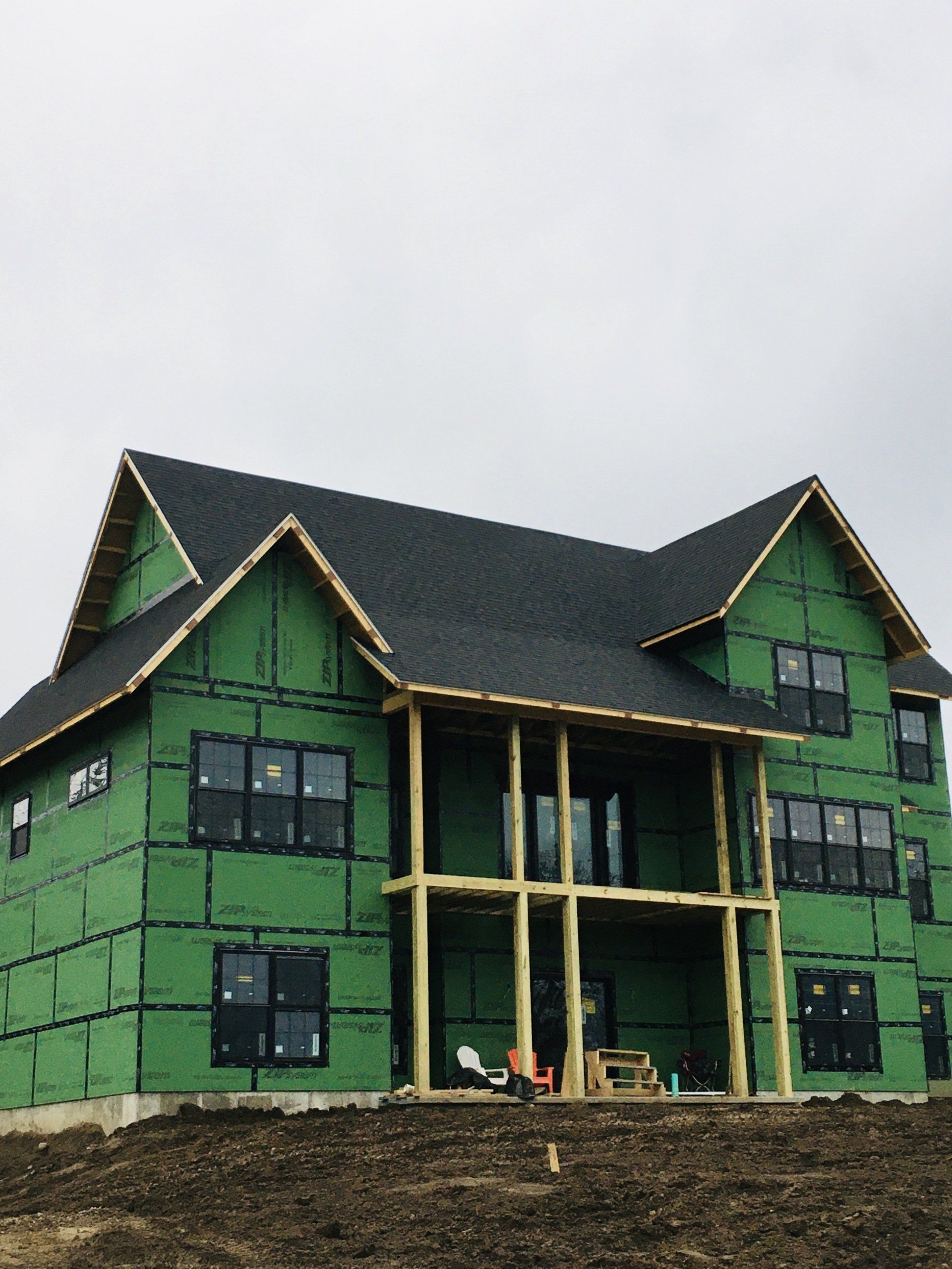 Green house under construction with dark roof and unfinished wooden front porch