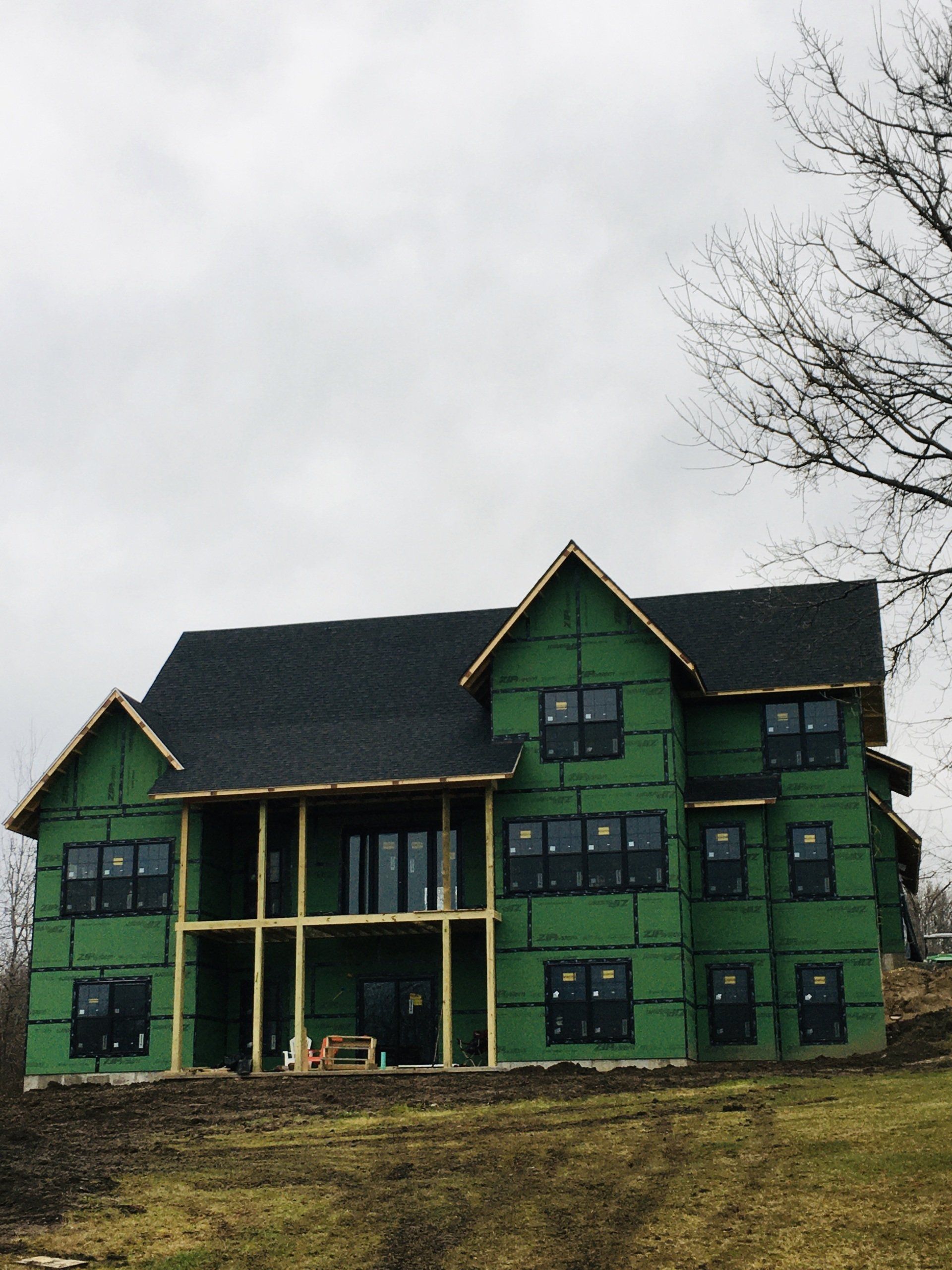 Green two-story house under construction with dark roof on a cloudy hillside
