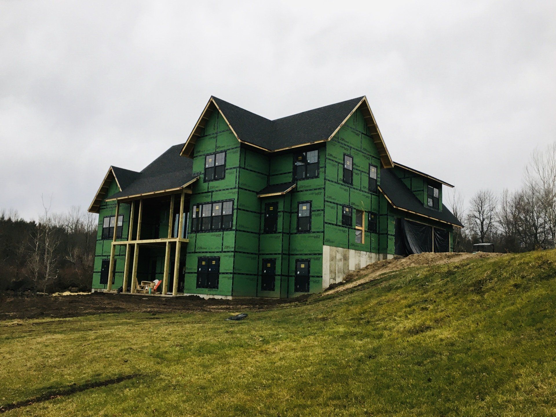 Green multi-story house under construction on a grassy slope under a cloudy sky