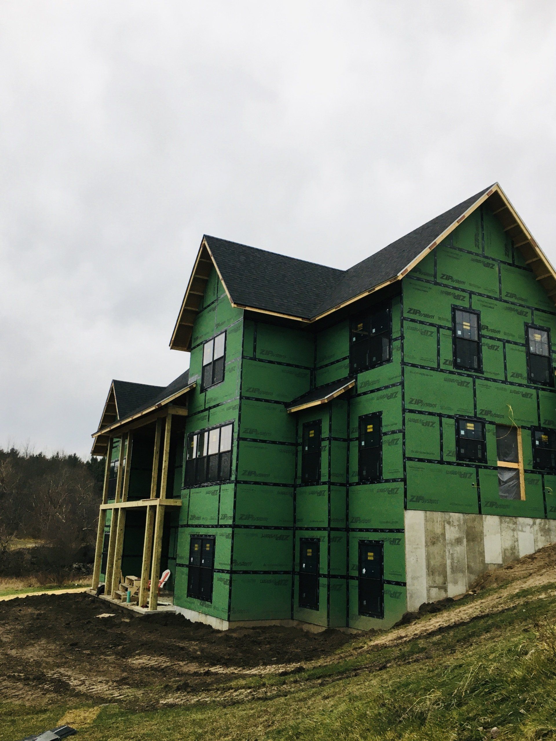 Green house under construction with exposed framing and partially unfinished roof on a cloudy day