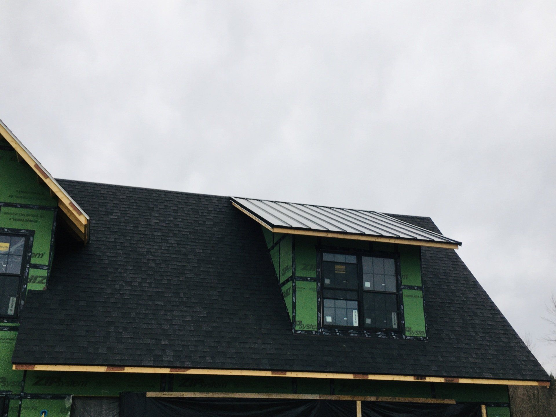 House roof with dark shingles and green dormer windows under a cloudy sky