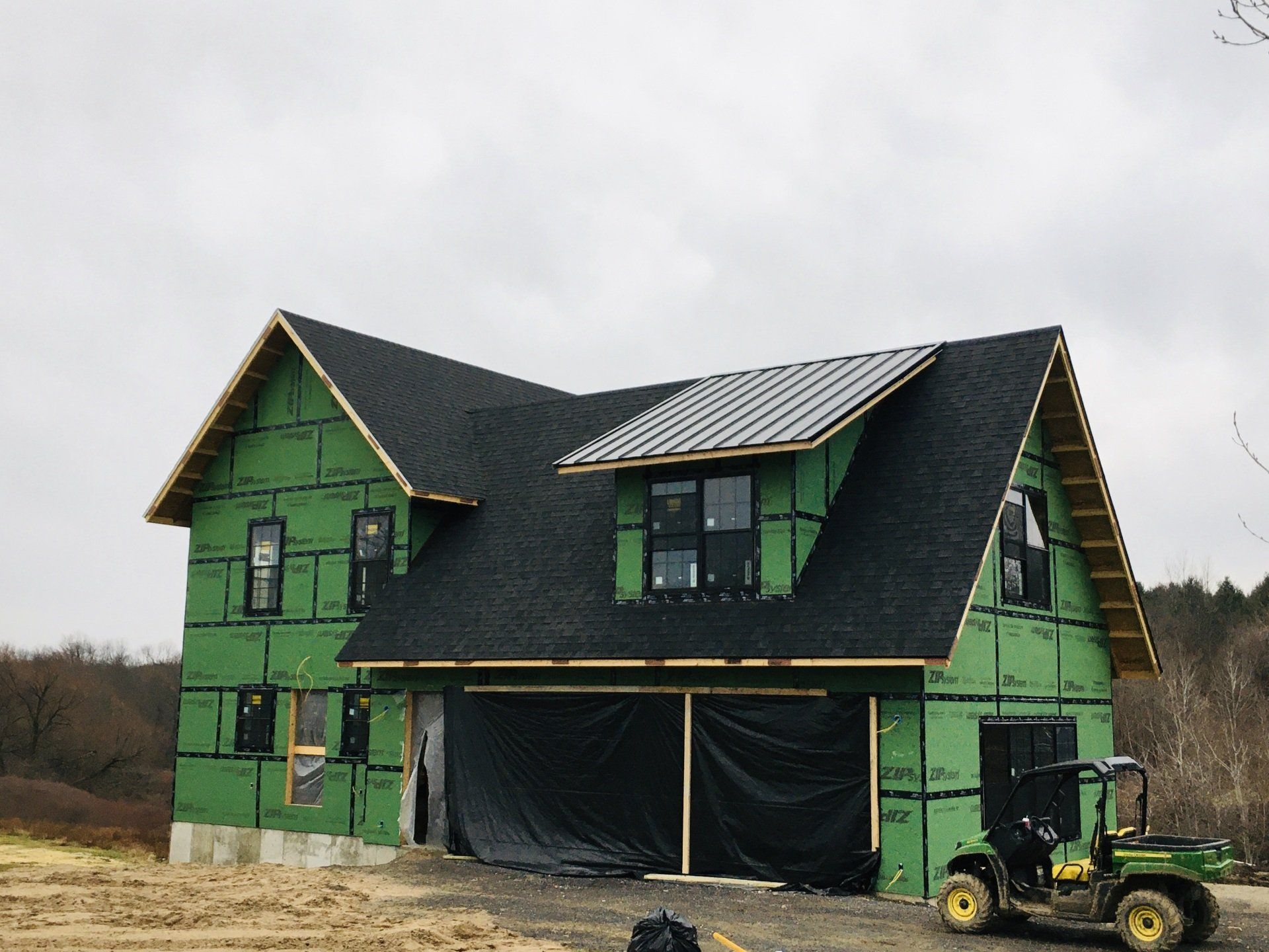 Green house under construction with dark roof, black wrap, and a small tractor in front