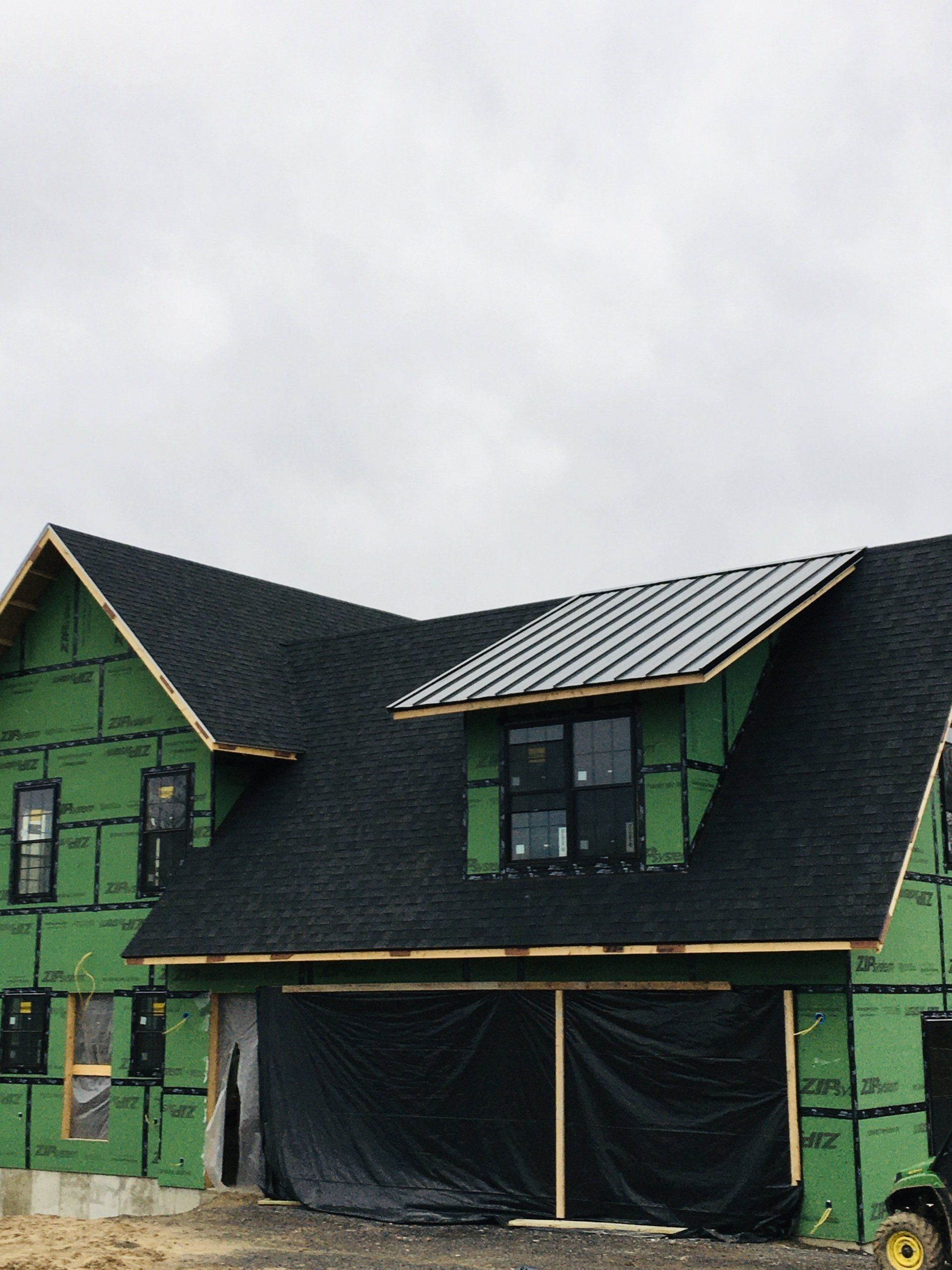 Green house under construction with black roof and covered front porch openings