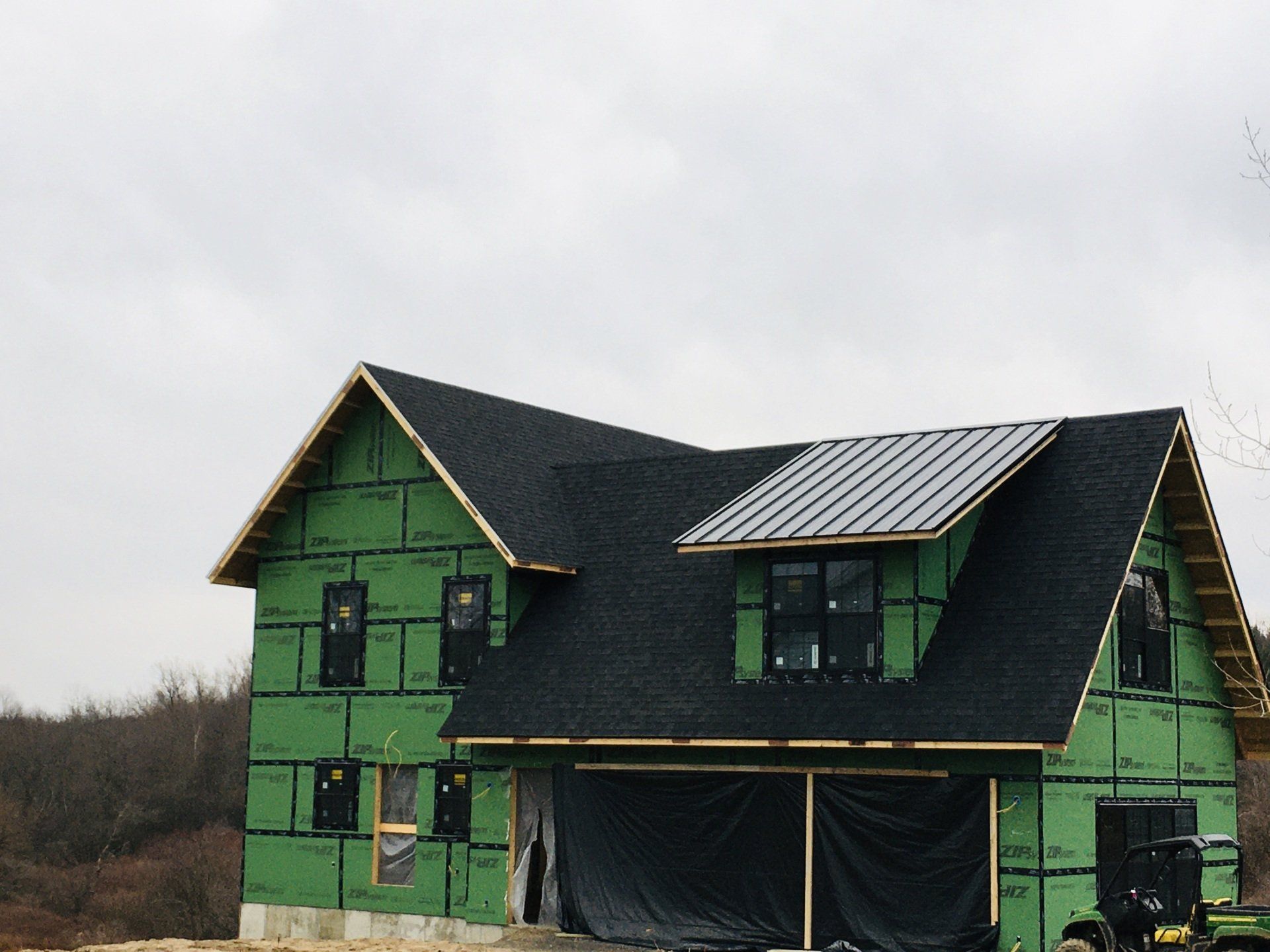 Green house under construction with black roof and exposed framing on a cloudy day
