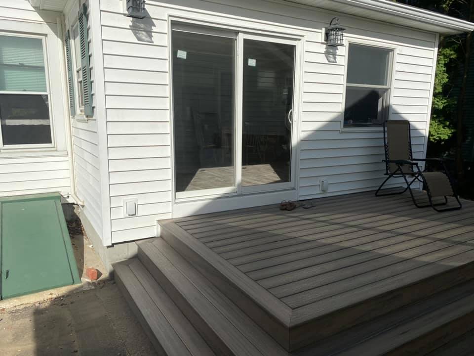 Back deck with gray steps, sliding glass doors, and patio chairs beside a white house
