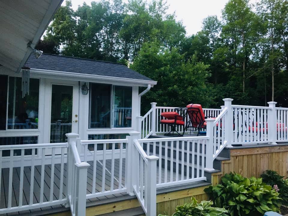 White-railed deck with red chairs beside a house, overlooking a wooded yard.