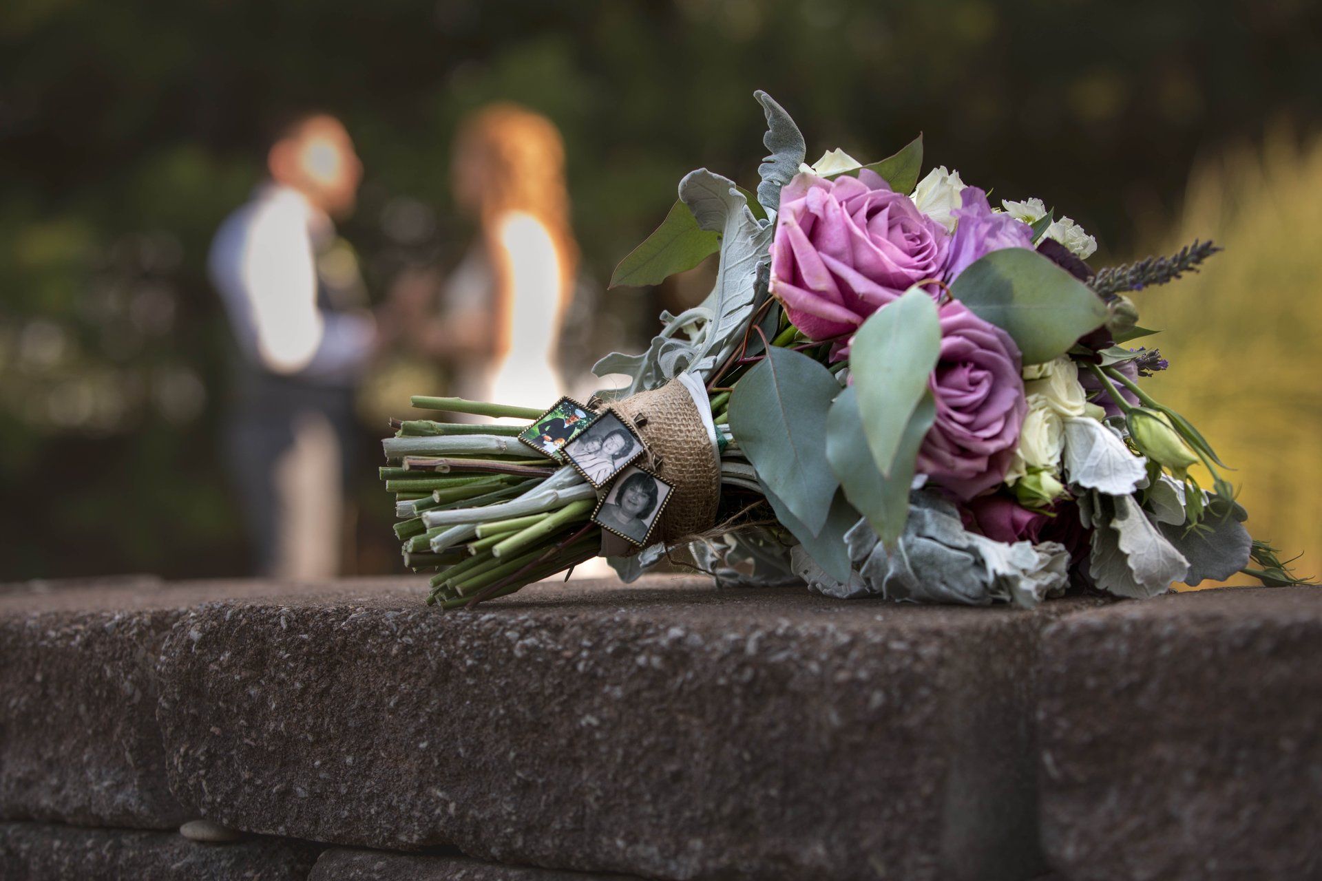 Bouquet of purple roses on a stone wall, blurred couple in background.