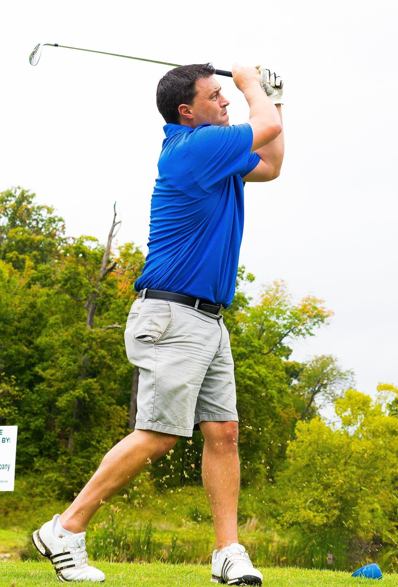 Man in blue shirt swings golf club on a green course.