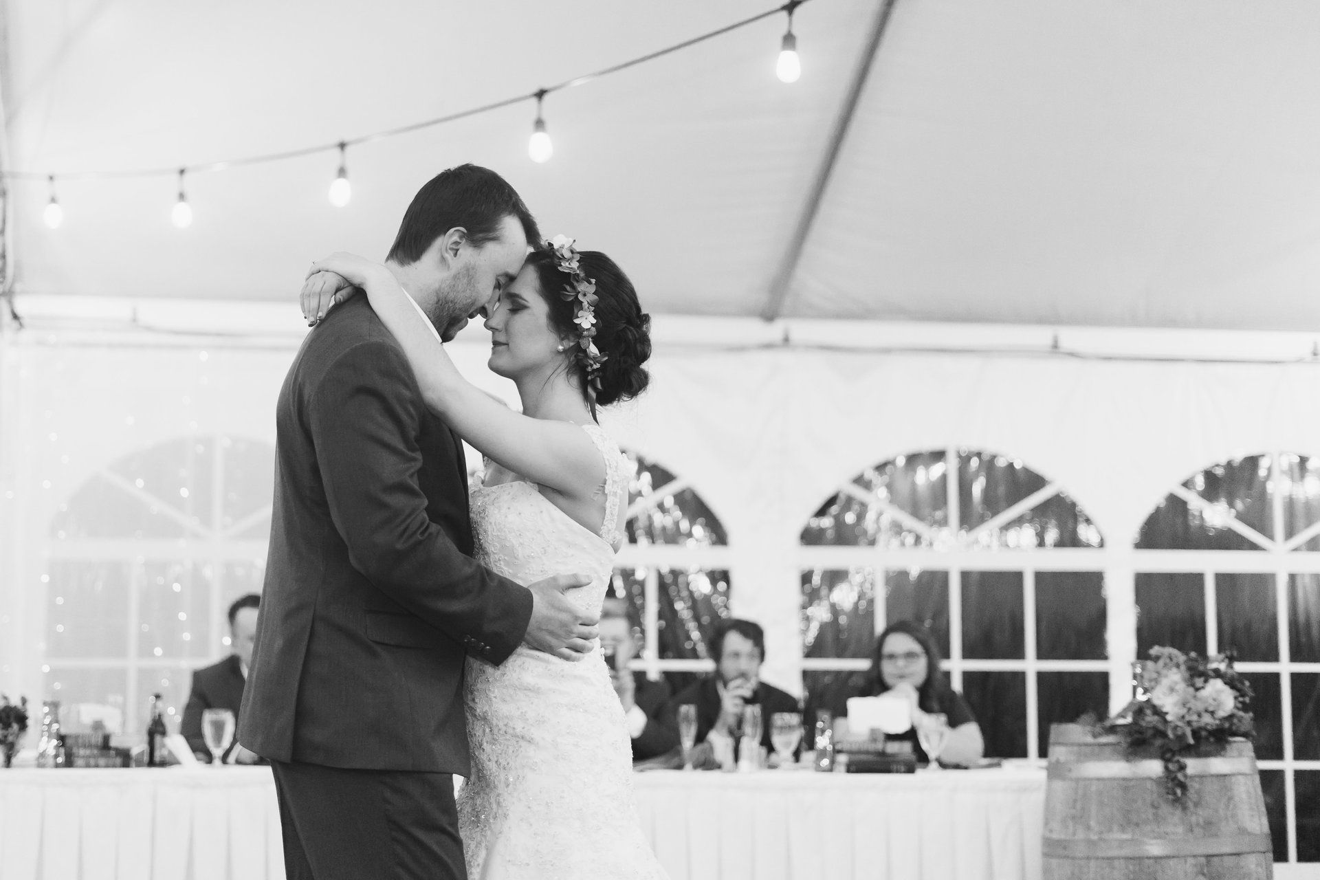 Bride and groom dance under a tent at their wedding reception. Soft lighting and guests in the background.