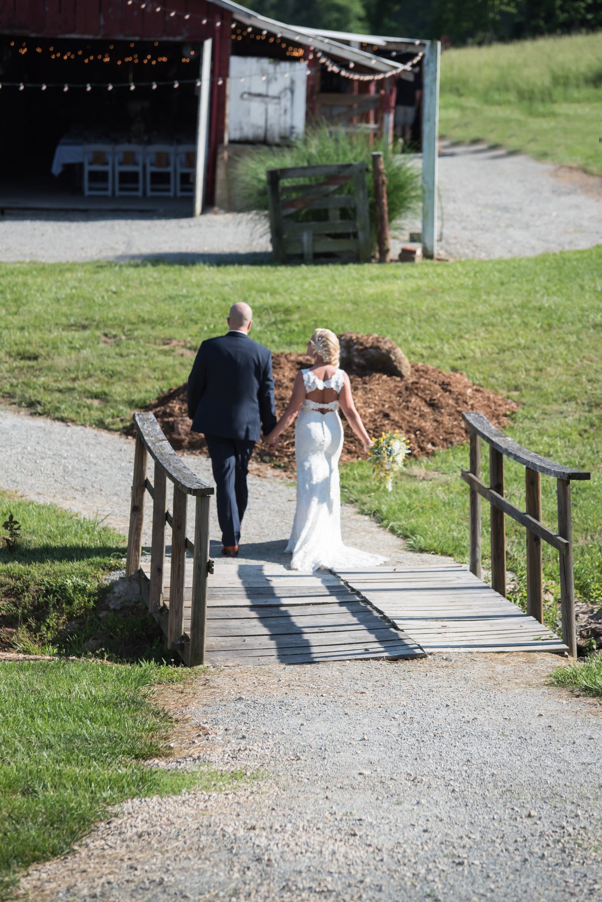Couple walking hand-in-hand across a wooden bridge toward a barn.