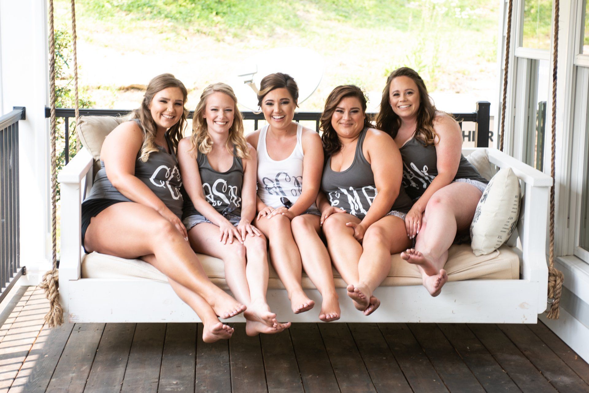 Five people sitting on a white swing on a porch, wearing tank tops and shorts.